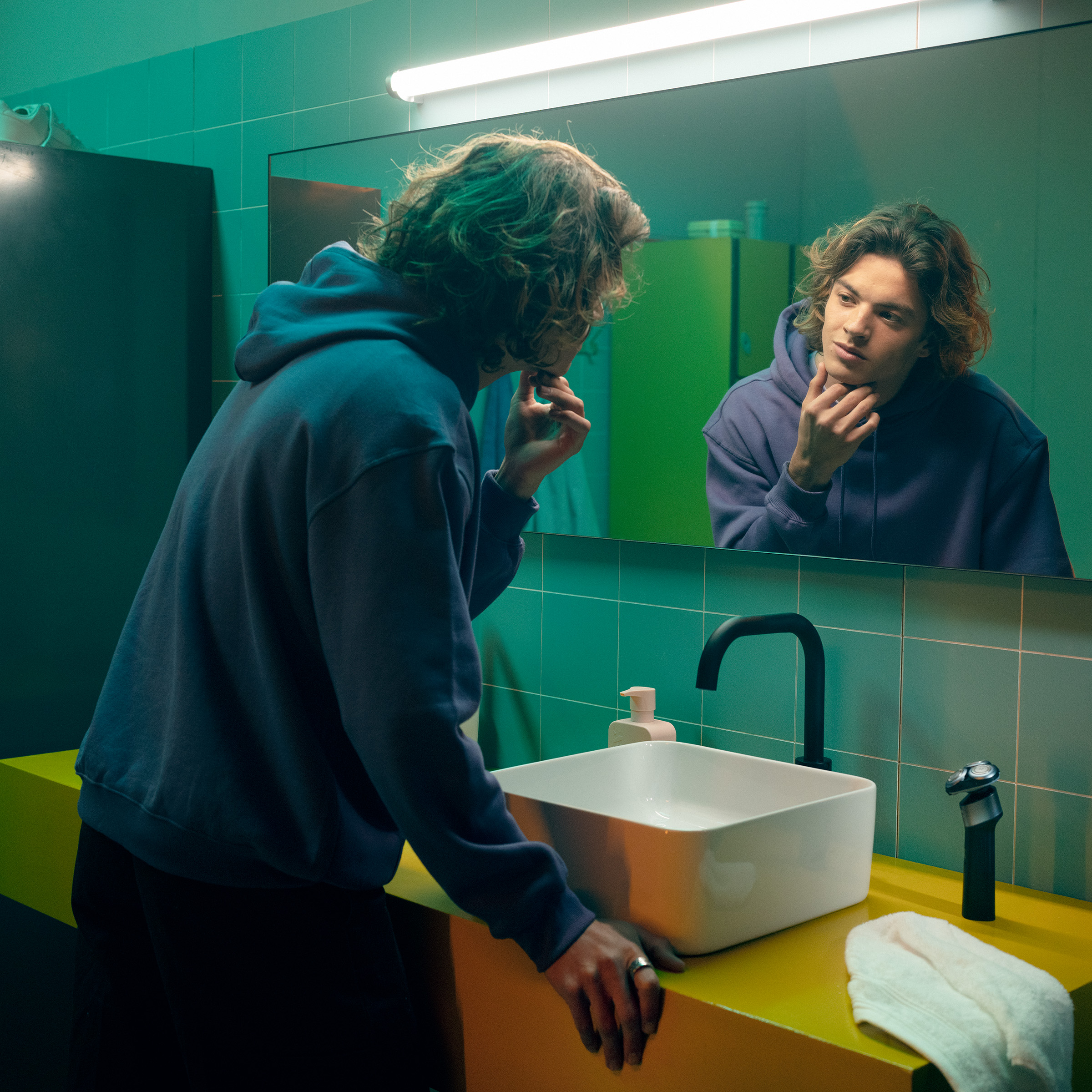 Młody mężczyzna z kręconymi włosami patrzy w łazienkowe lustro.