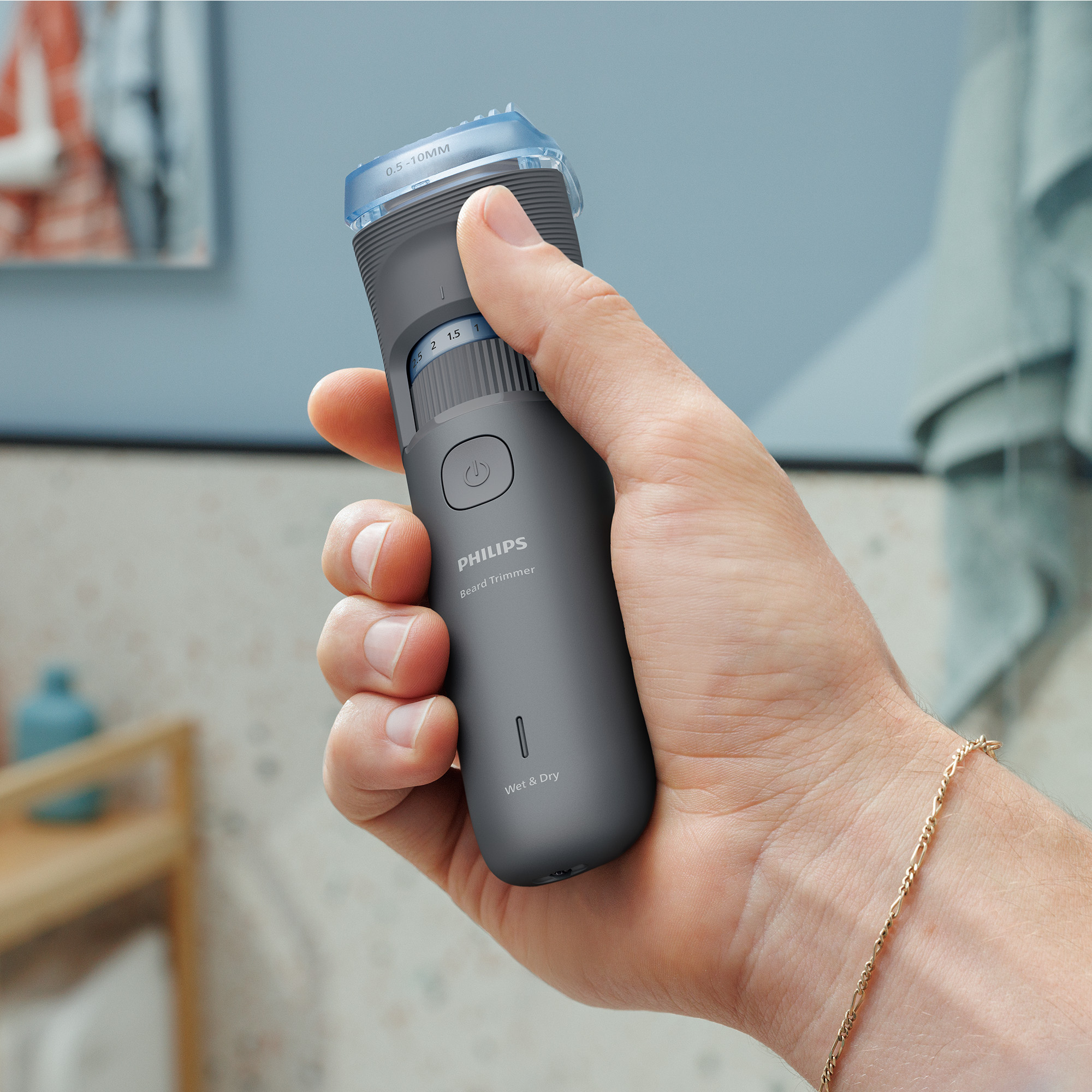 Dłoń trzyma szary trymer do brody Philips z niebieską nasadką. W tle łazienka.