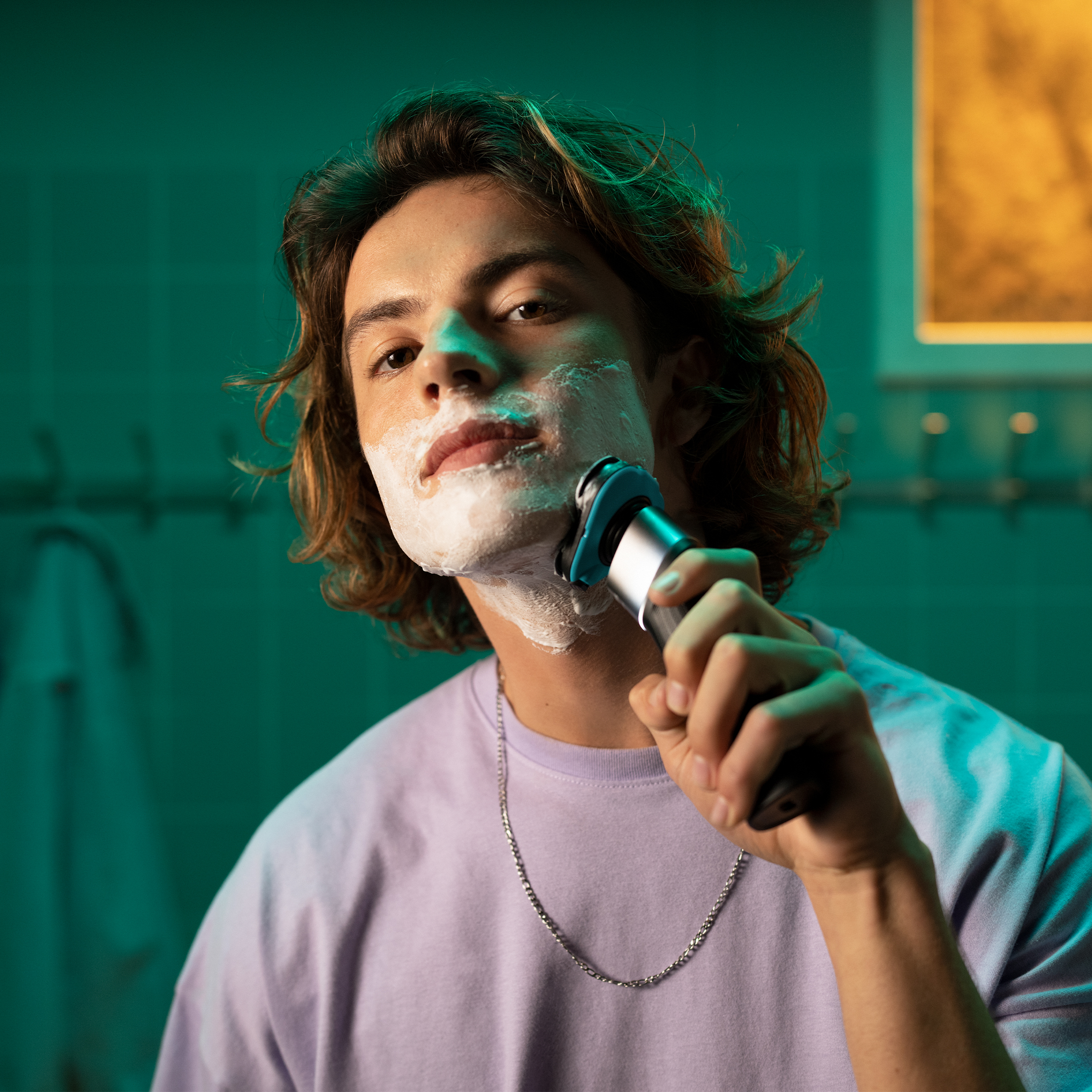 Młody mężczyzna z pianką do golenia na twarzy goli się golarką elektryczną.