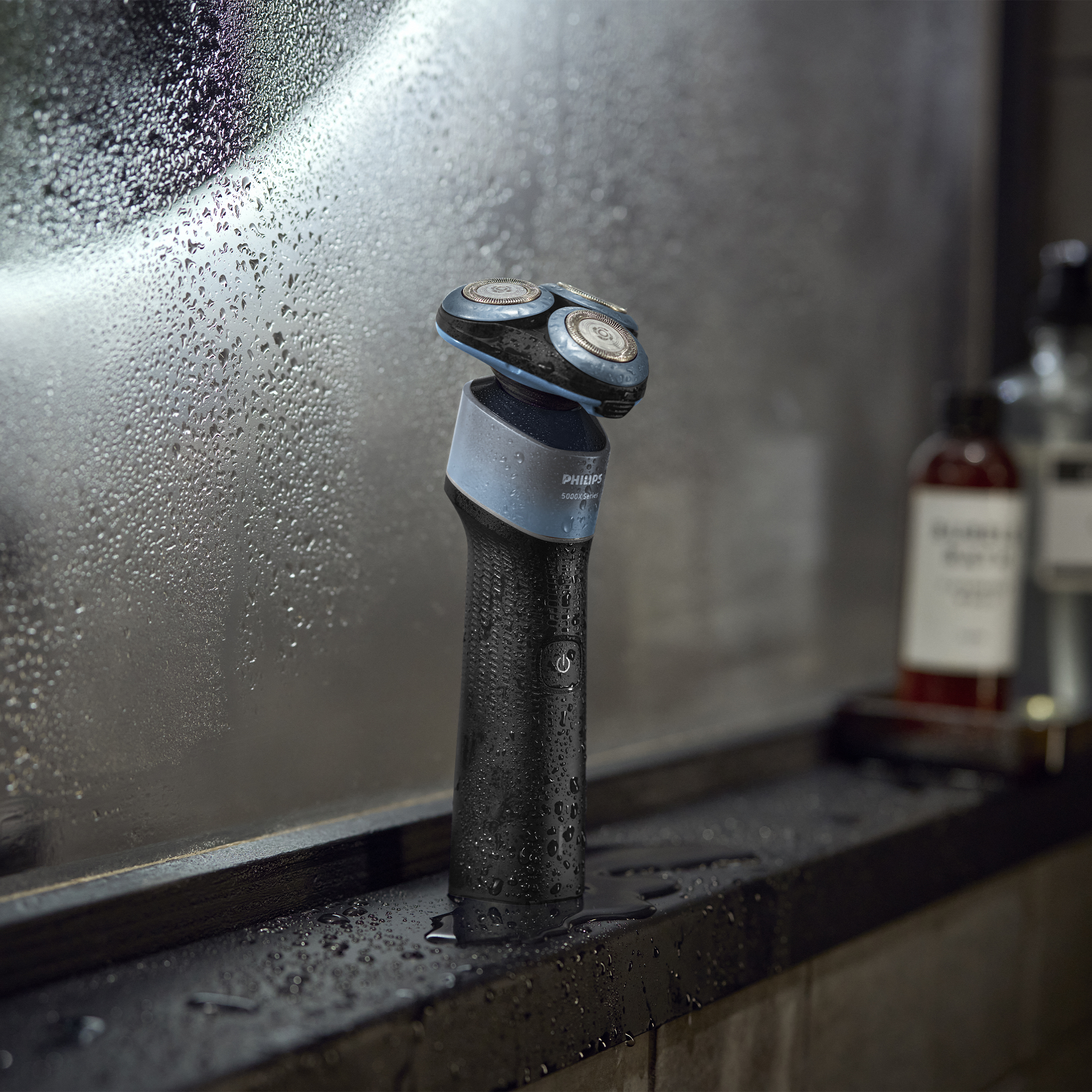 Mokra golarka Philips stoi na ciemnej powierzchni z kroplami wody.