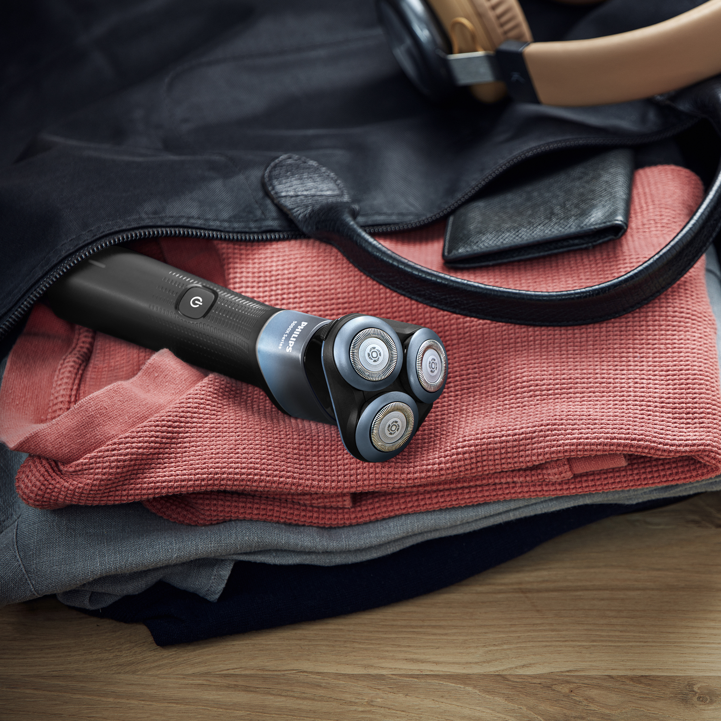 Czarna maszynka do golenia Philips leży na ubraniach w torbie.