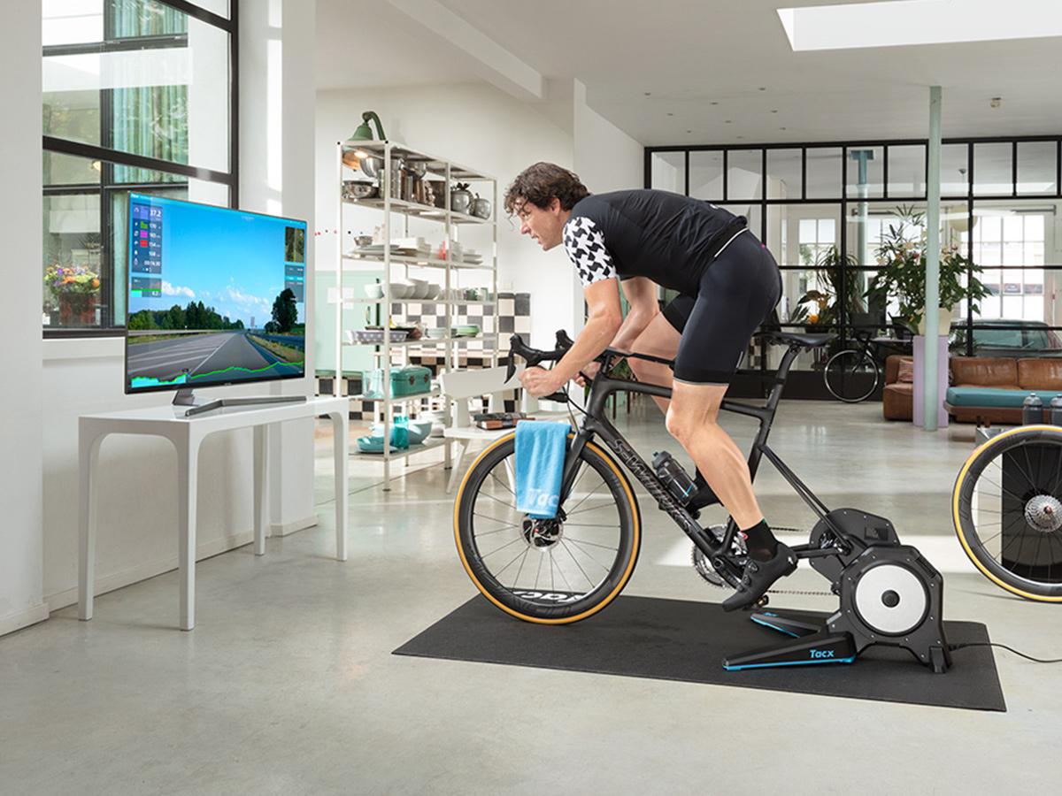 Mann auf einem Heimtrainer im Wohnzimmer, der vor einem Fernsehbildschirm fährt.