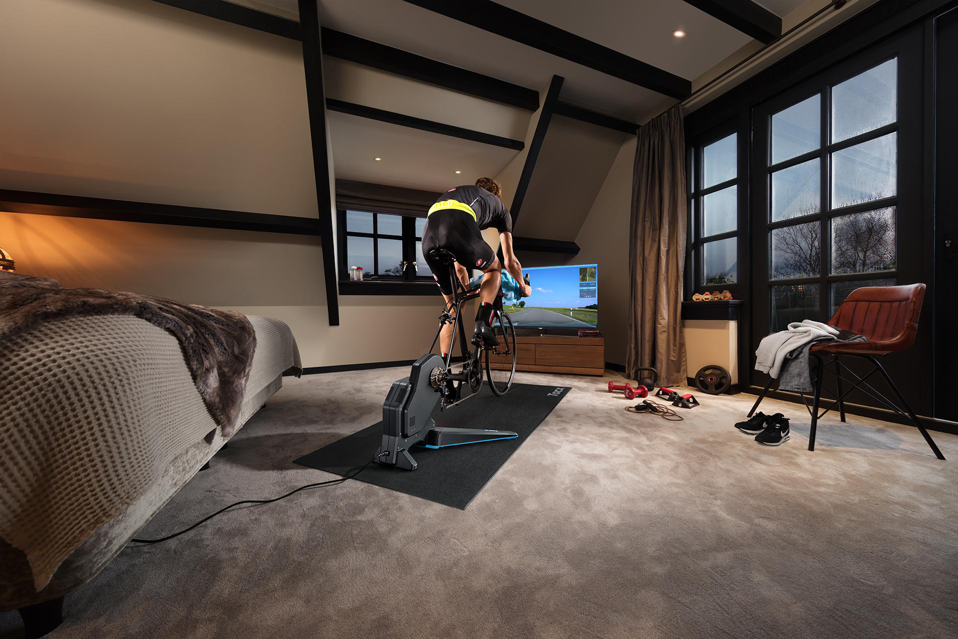 Mann auf Indoor-Fahrrad vor Fernseher in einem Schlafzimmer.