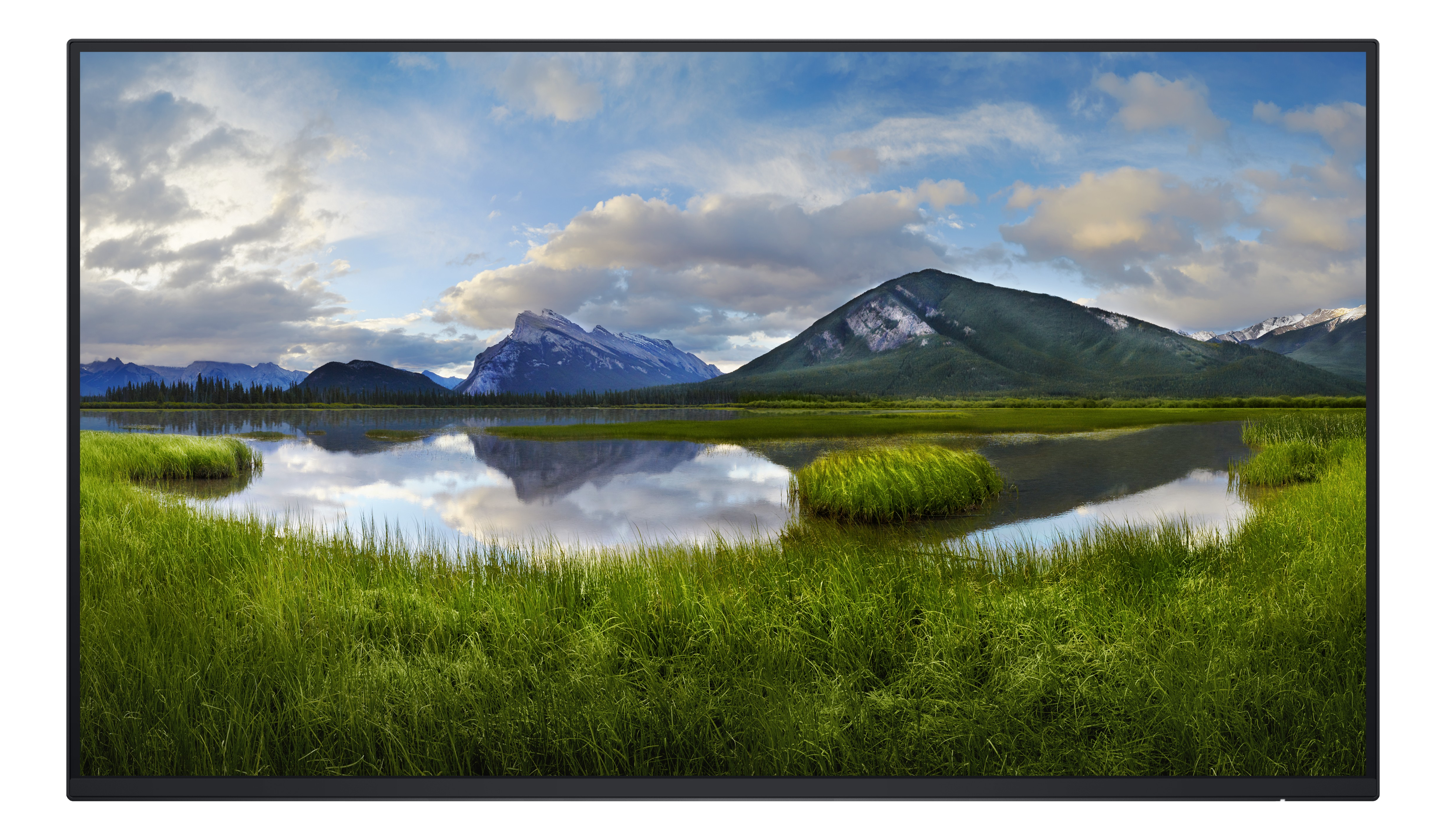 Des prairies vertes et des montagnes se reflètent dans un lac calme sous un ciel nuageux.