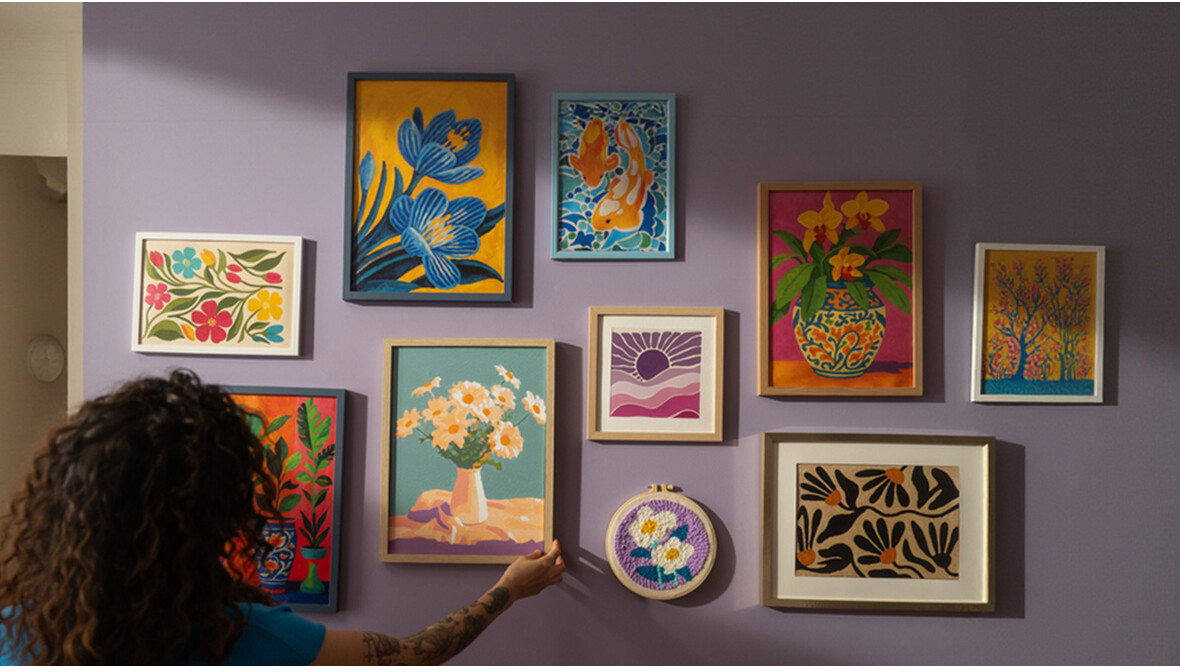 Opere d'arte colorate pendono da un muro viola, con una donna che le sistema.