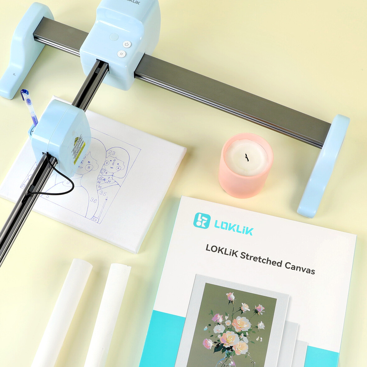 Un plotter con penna su tela con disegno, accanto candela e libro.