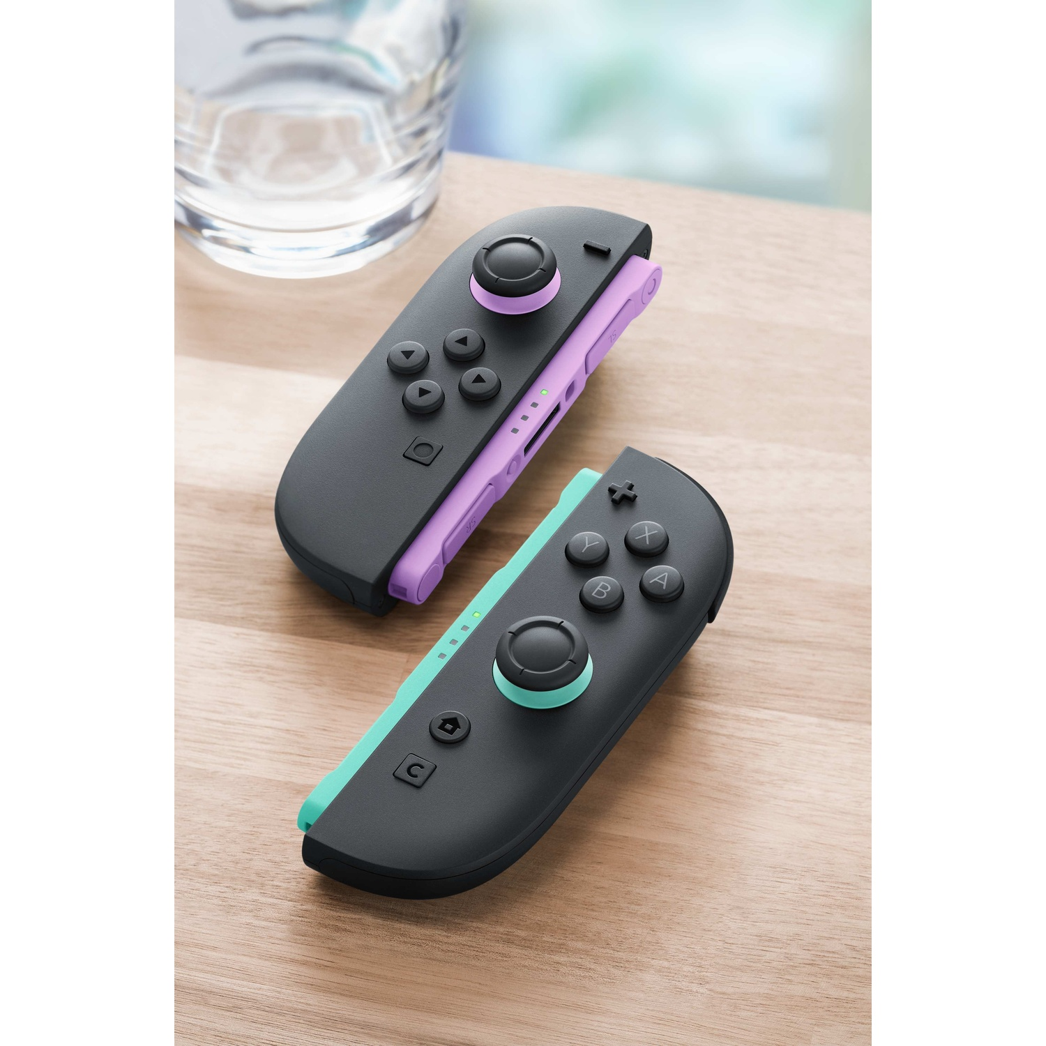 Due controller scuri su tavolo di legno, uno viola, uno verde menta.
