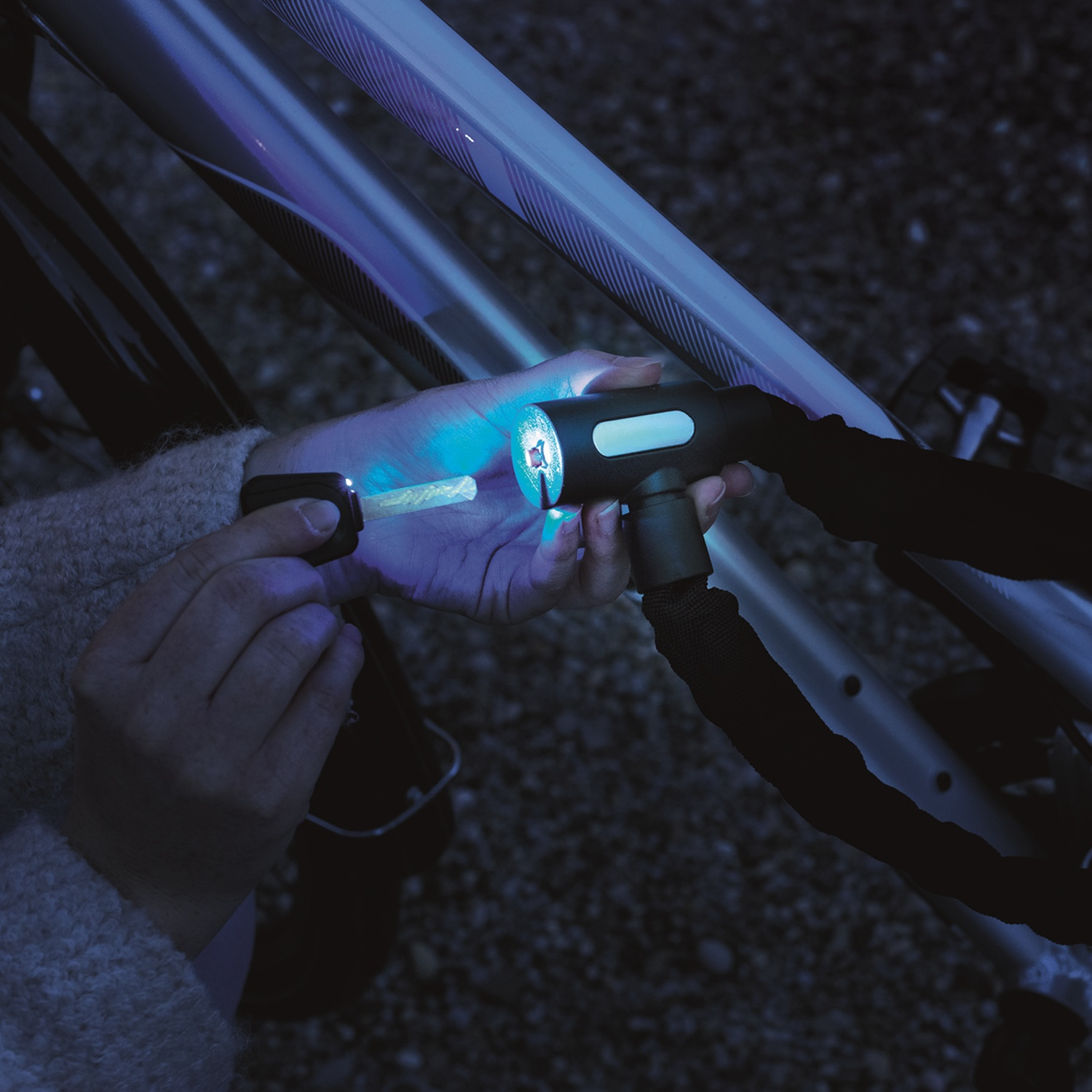 A hand holds a key emitting blue light to unlock a bicycle lock.