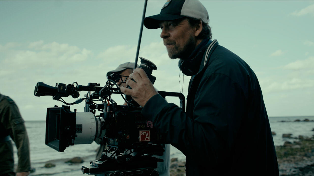 Ein Filmemacher bedient eine große Kinokamera an einem felsigen Ufer am Meer.