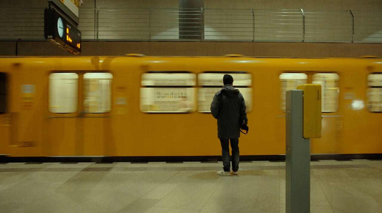 Eine Person wartet auf einem Bahnsteig auf einen gelben Zug.