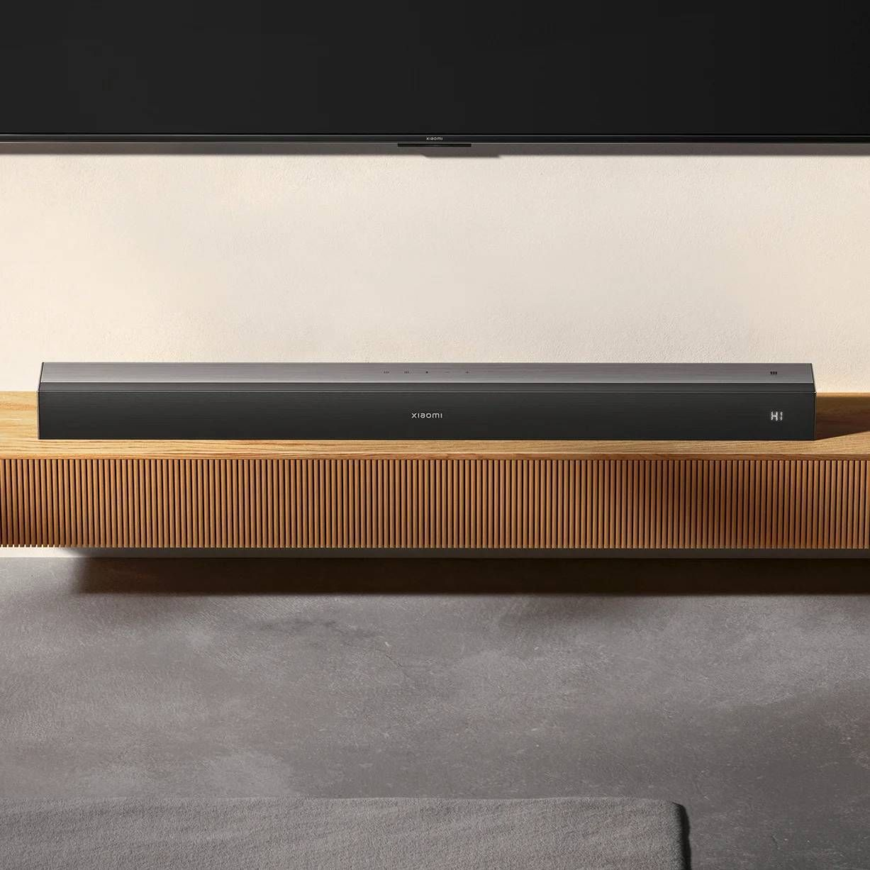 Barre de son Xiaomi noire sur étagère en bois devant TV et mur.