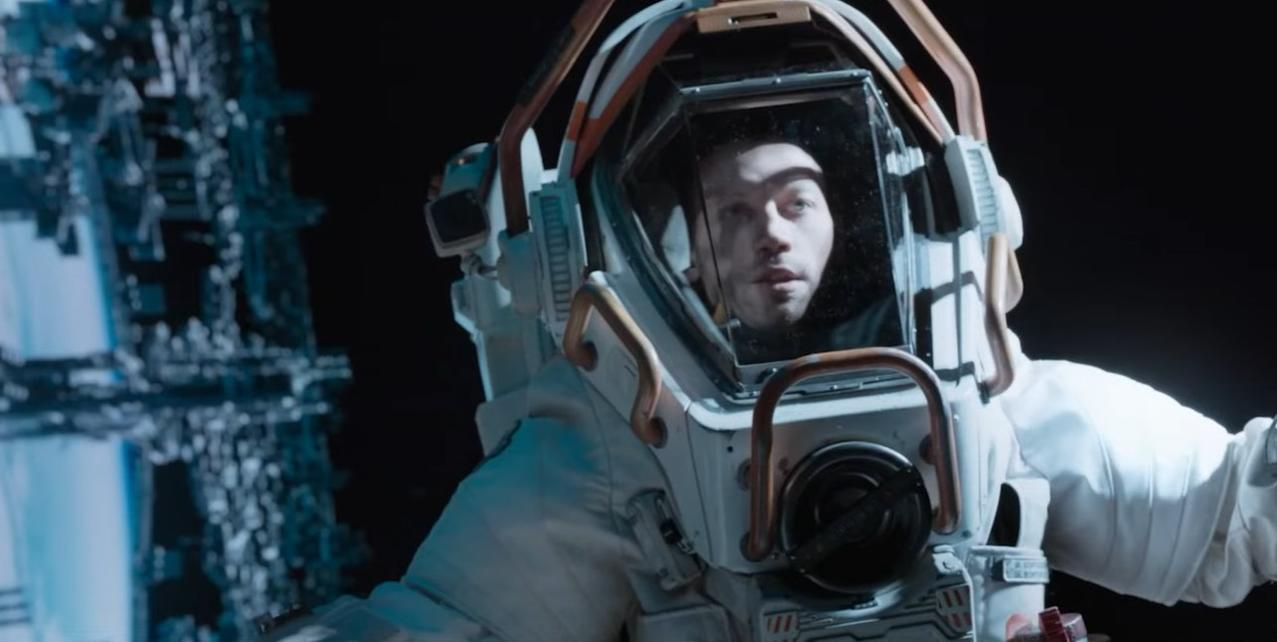 Ein Astronaut im Raumanzug blickt aus dem Visier, ein Raumschiff im Hintergrund.