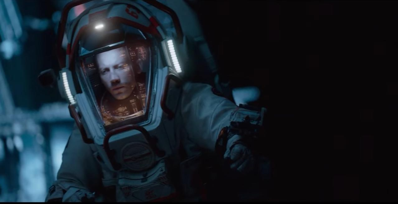Ein Mann im Raumanzug mit Helm schaut nach rechts, dunkler Hintergrund.