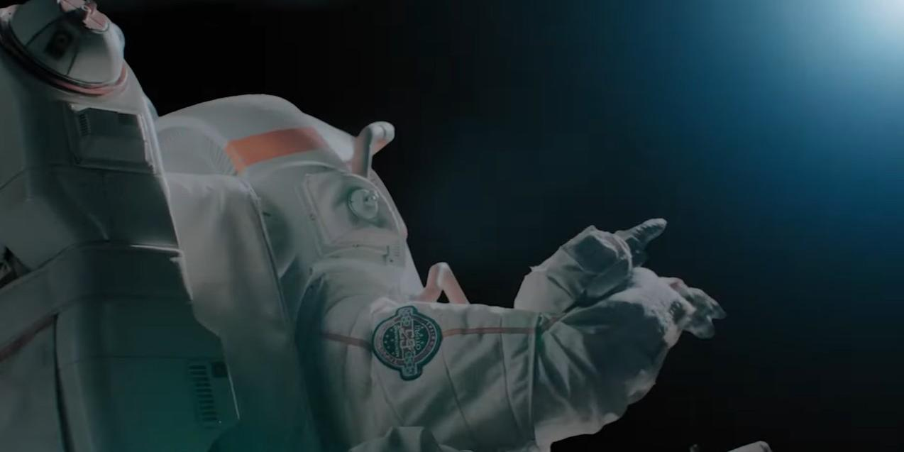 Ein Astronaut in einem weißen Raumanzug mit orangen Akzenten, der im Dunkeln auf etwas zeigt.