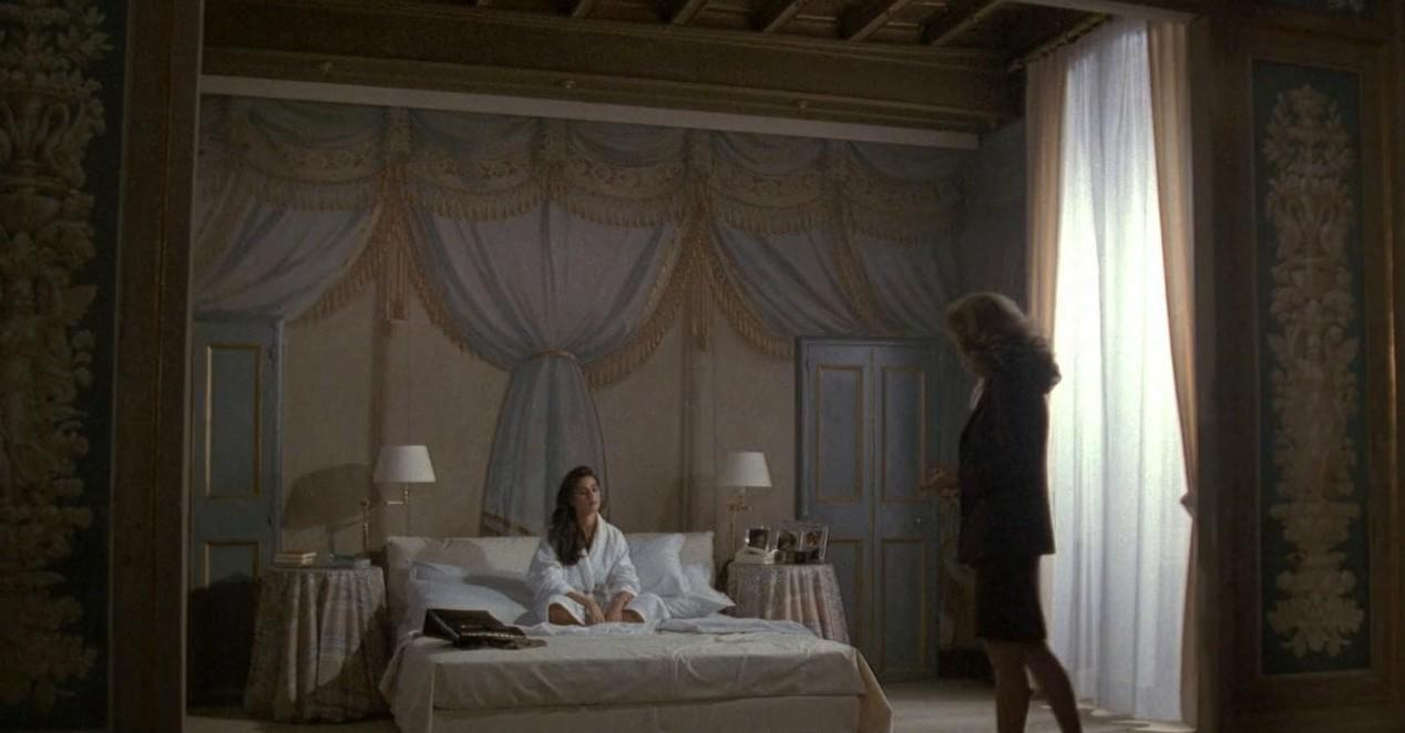 Eine Frau im Bademantel sitzt auf einem Bett, eine andere Frau steht daneben.
