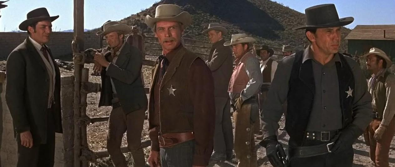 Männer in Cowboykleidung stehen vor einer Hütte im Westen.
