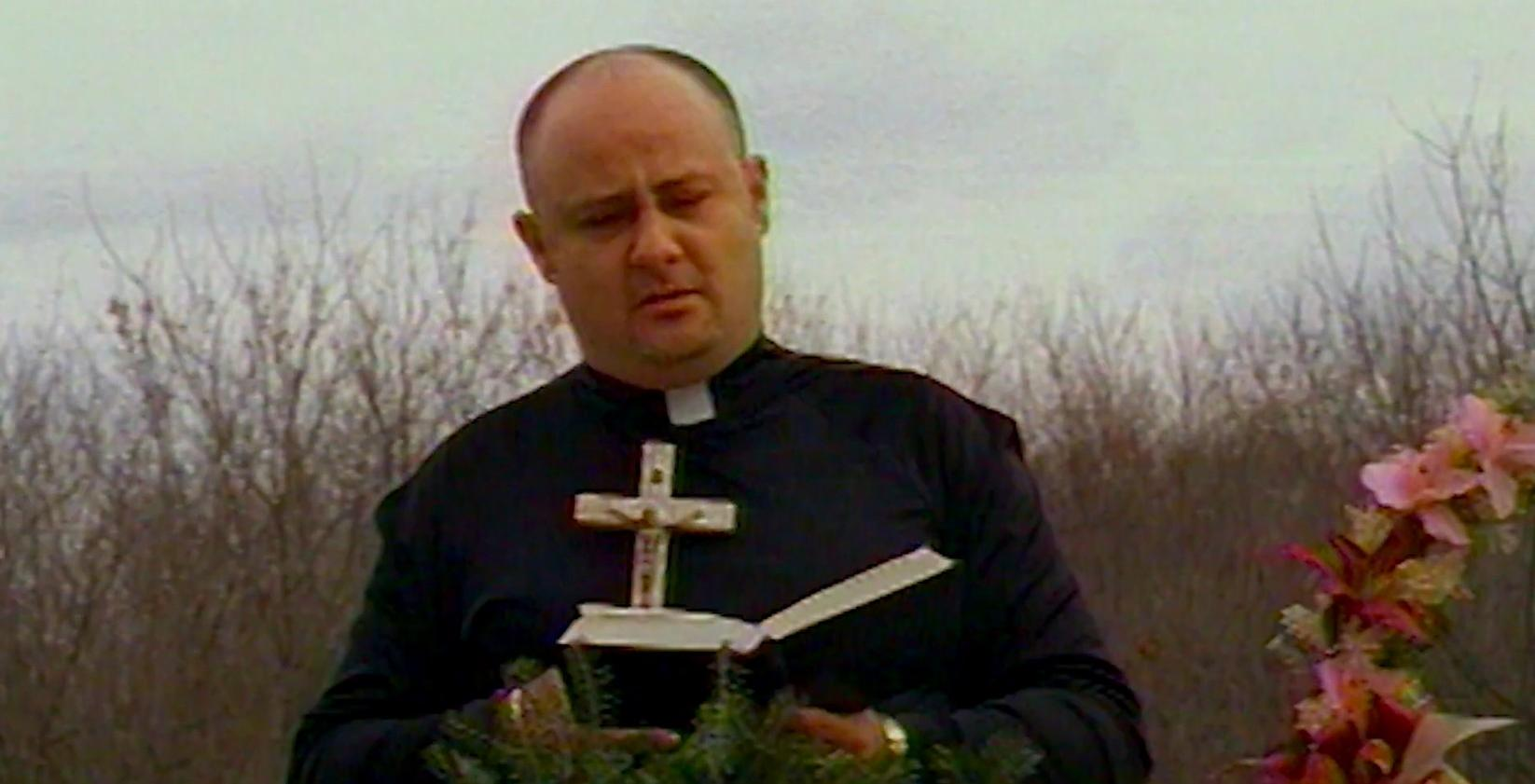 Ein Geistlicher in schwarzer Soutane mit Kreuz liest aus einem Buch.