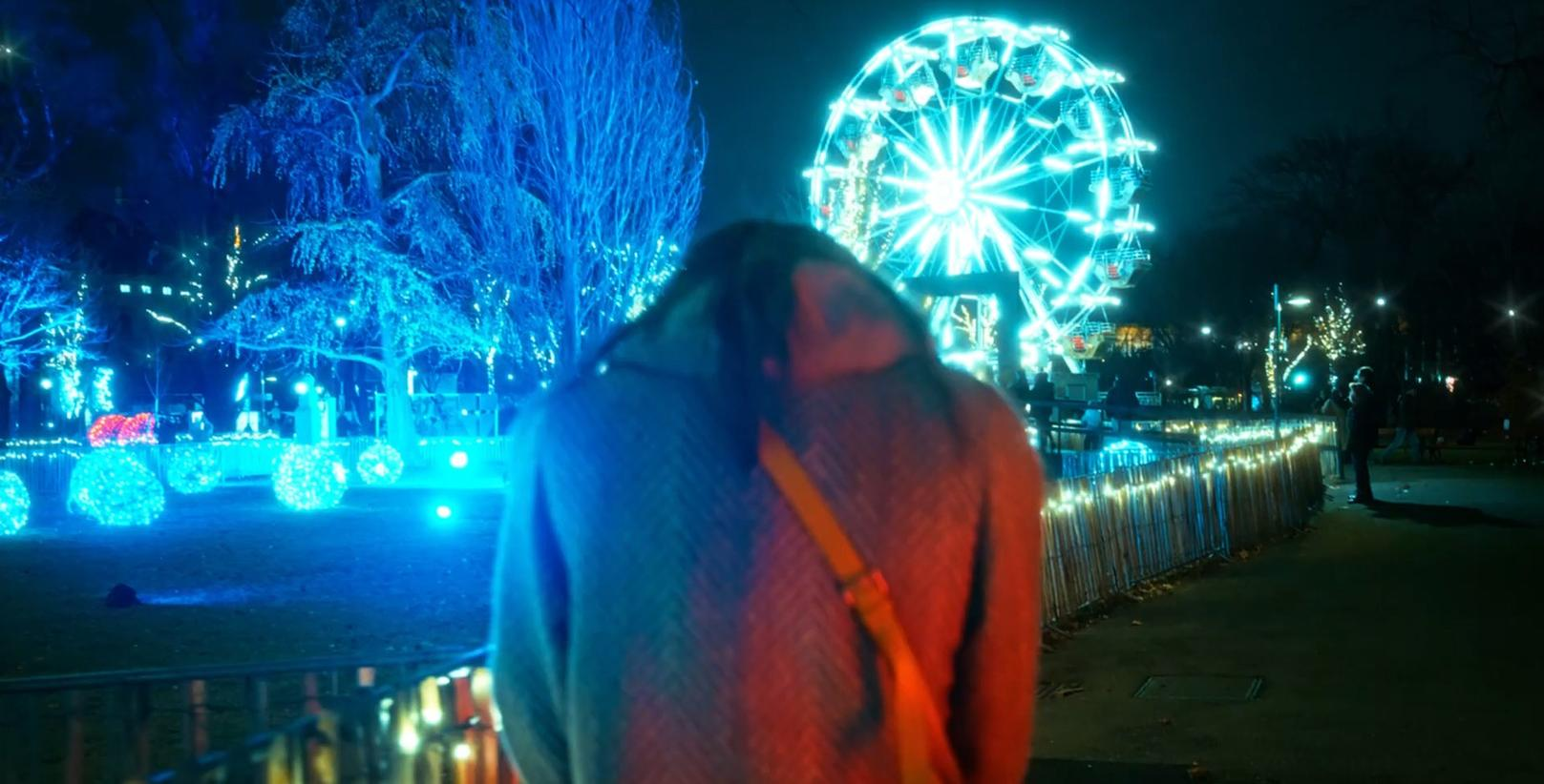 Eine Person mit Rucksack steht vor einem beleuchteten Riesenrad und Bäumen.