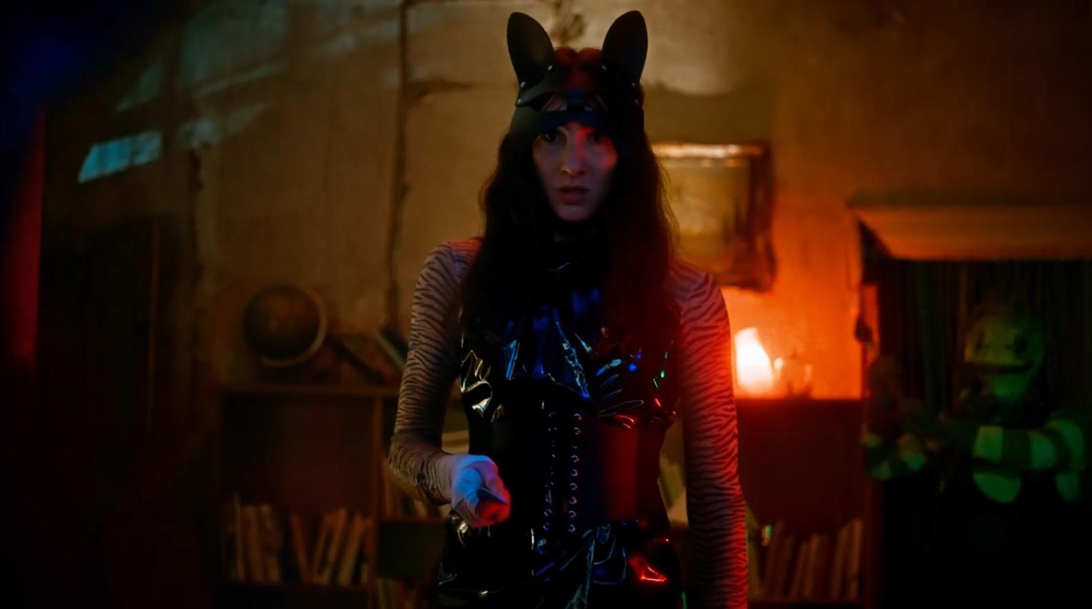 Eine Frau trägt eine schwarze Katzenmaske und ein glänzendes Outfit.