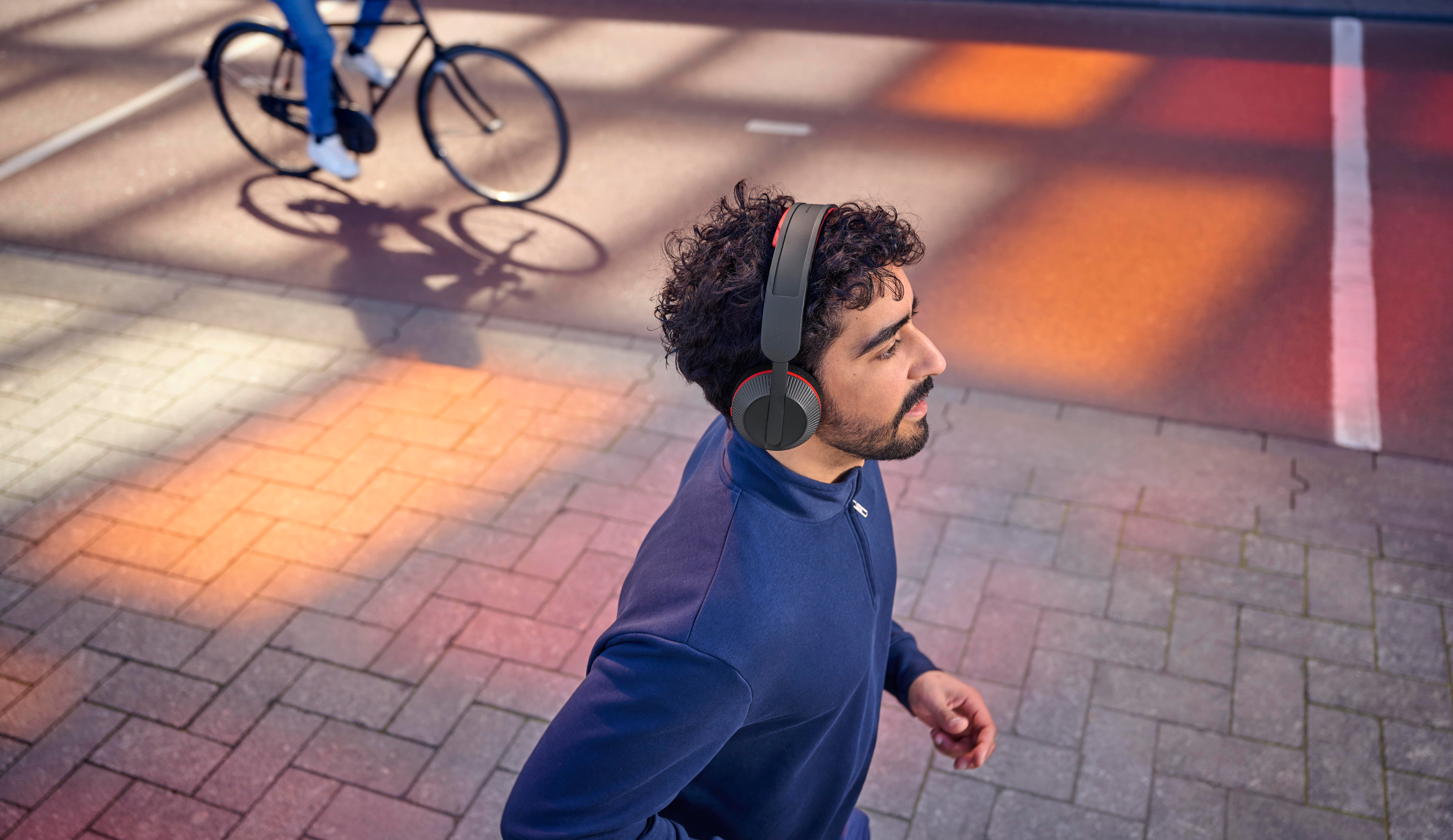 Mann mit Kopfhörern geht im Freien, Radfahrer im Hintergrund.