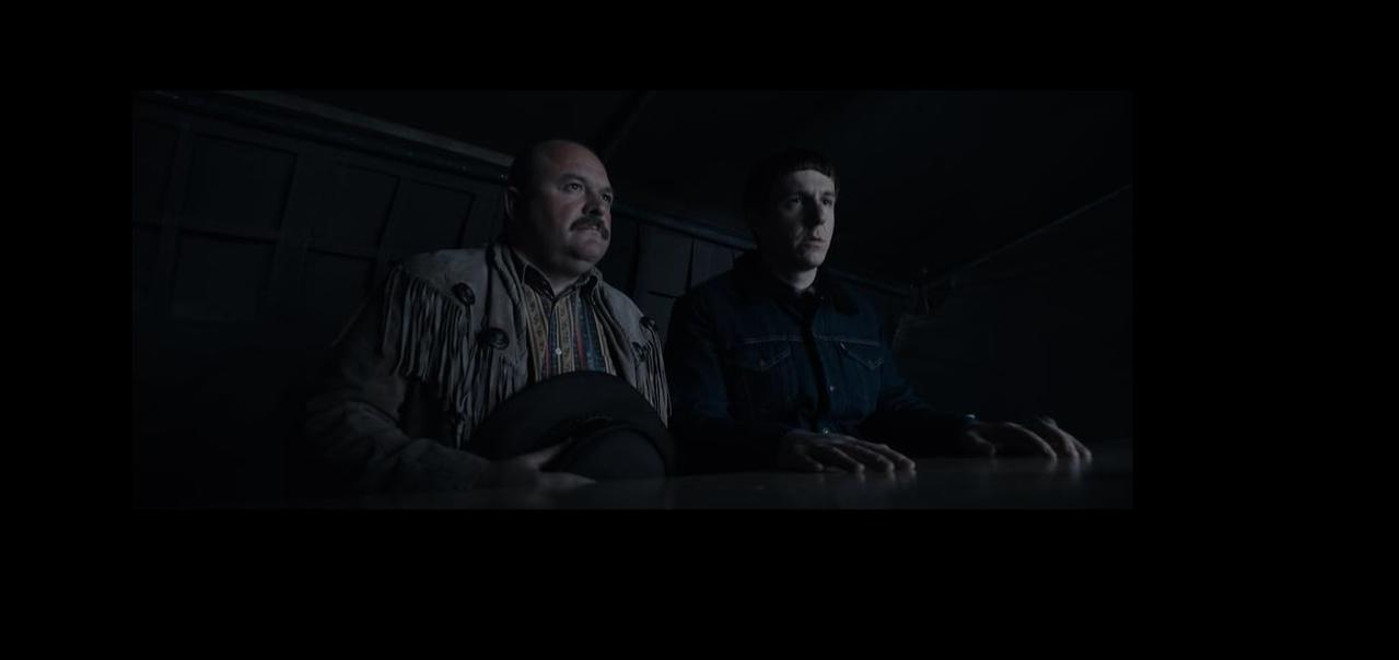 Zwei Männer sitzen an einem Tisch. Einer trägt eine Fransenjacke, der andere eine Jeansjacke.