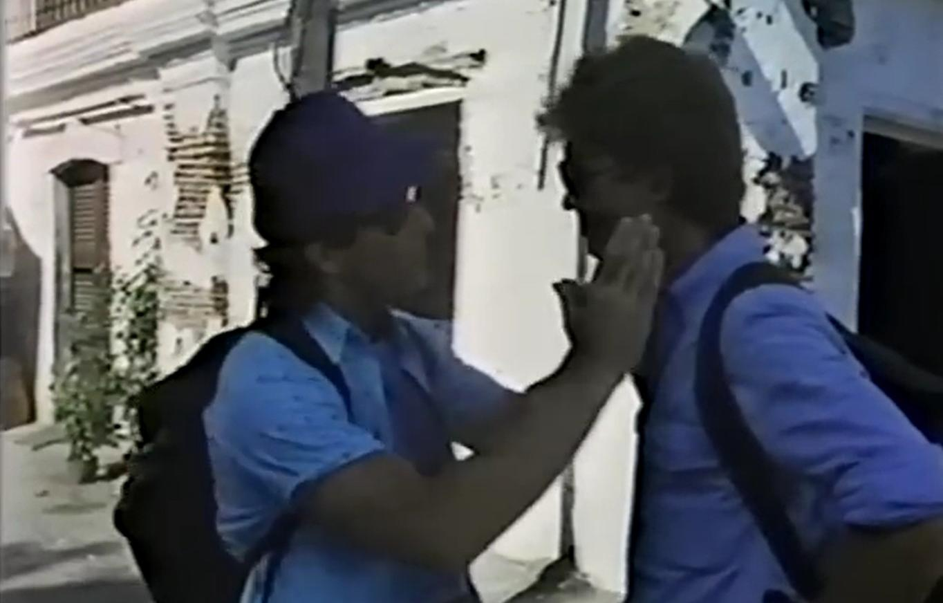 Zwei Personen in blauen Hemden stehen sich gegenüber. Eine Person hält ihre Hand vor das Gesicht der anderen.