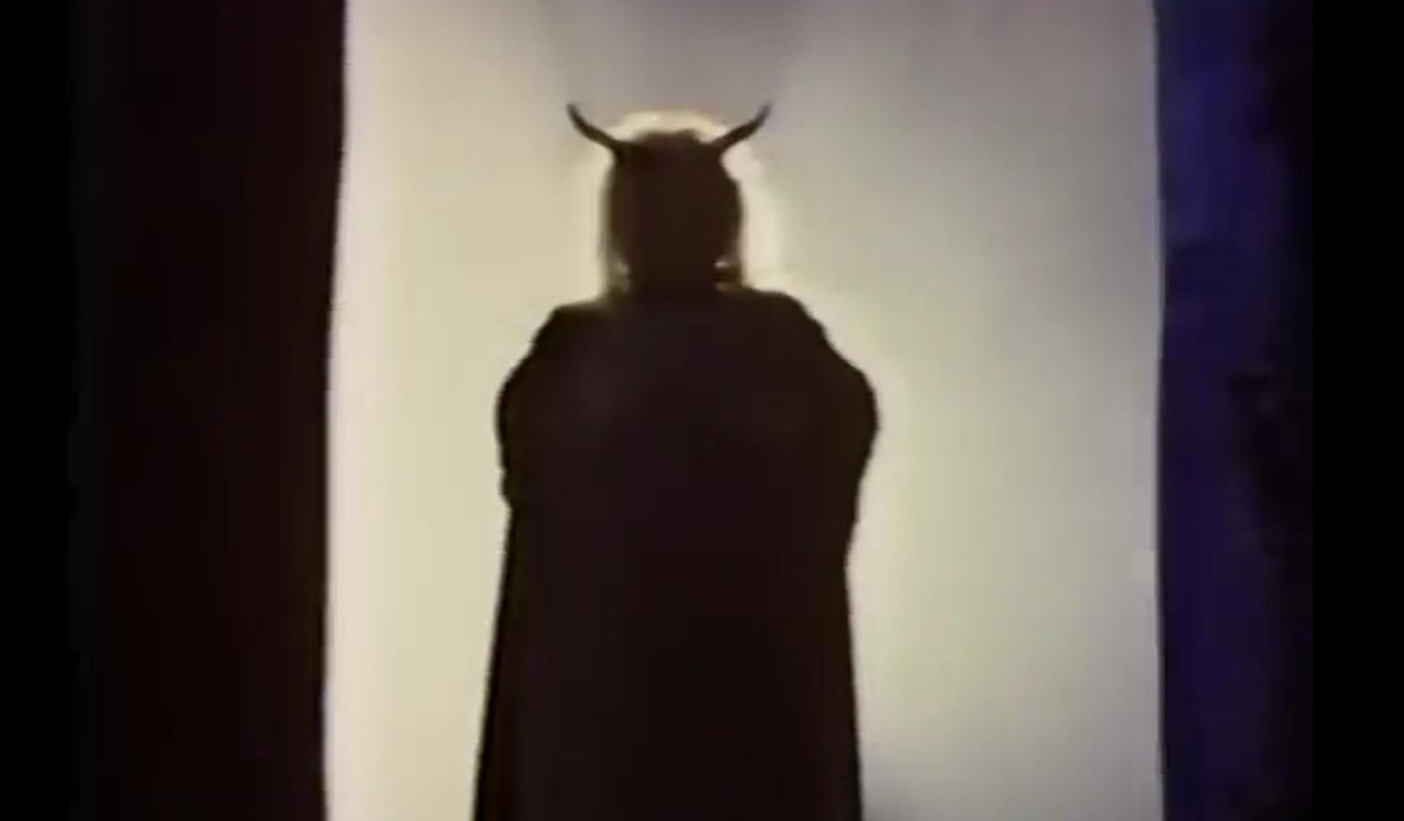 Silhouette einer Person mit Teufelshörnern und Umhang vor hellem Hintergrund.