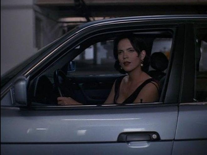 Eine Frau mit dunklem Haar sitzt am Steuer eines Autos und blickt nach rechts.