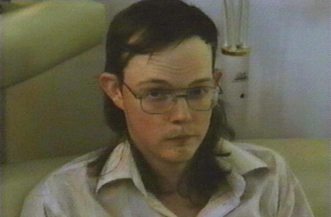 Ein Mann mit Brille und Langhaarfrisur trägt ein gestreiftes Hemd.