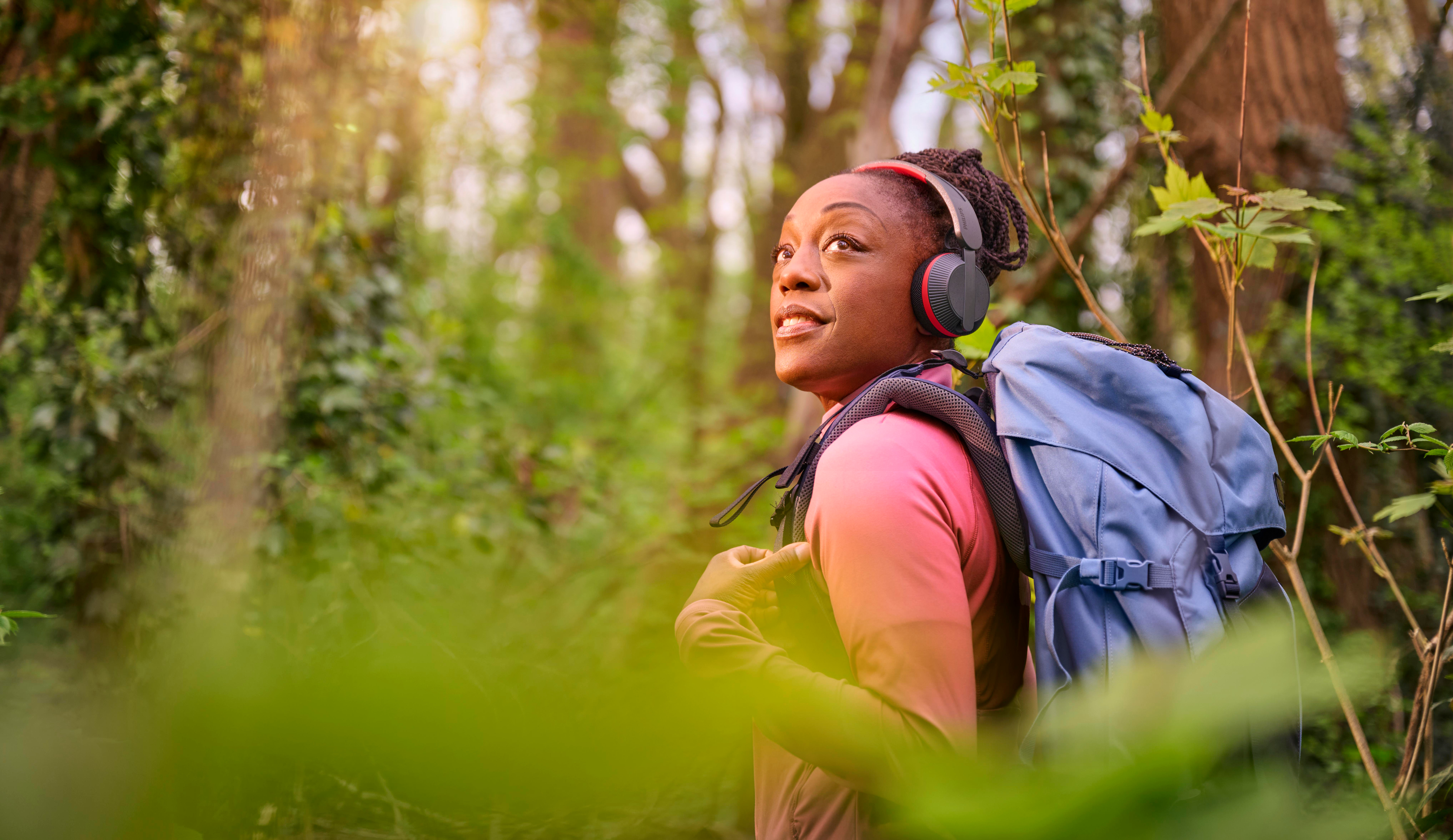 Eine Frau mit Kopfhörern und Rucksack wandert im Wald.
