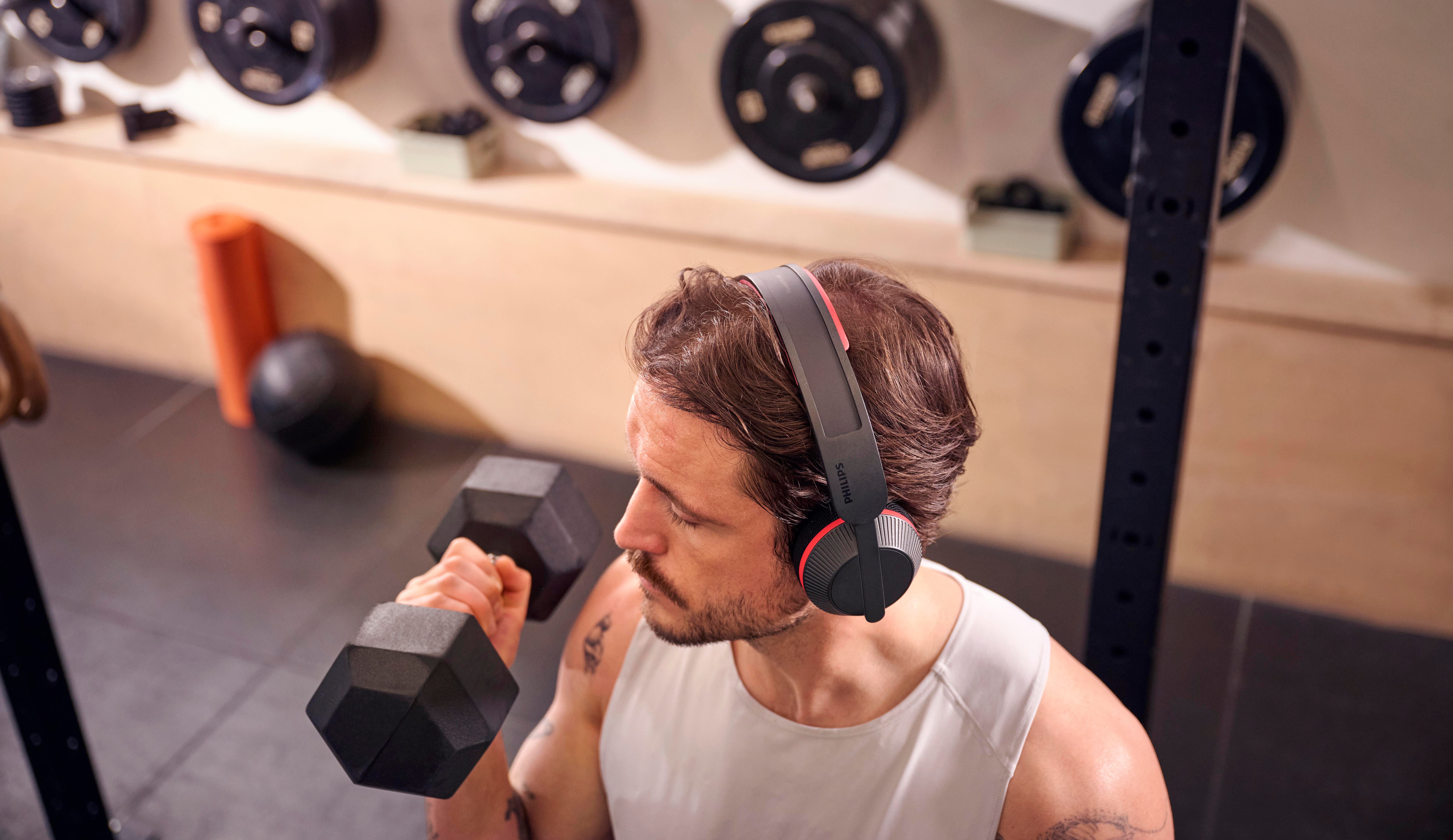 Mann mit Kopfhörern hebt eine Hantel im Fitnessstudio.