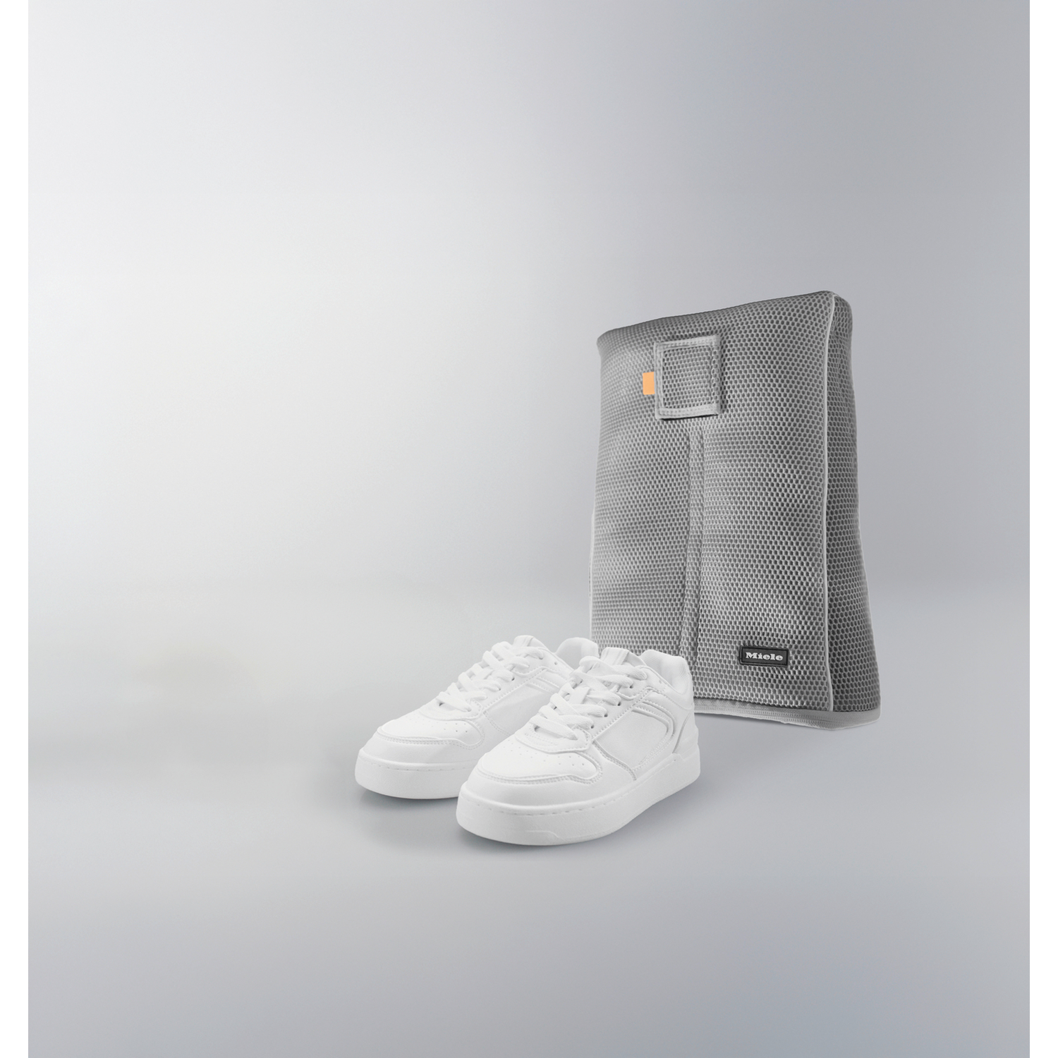 Twee witte sneakers naast een grijze Miele waszak.