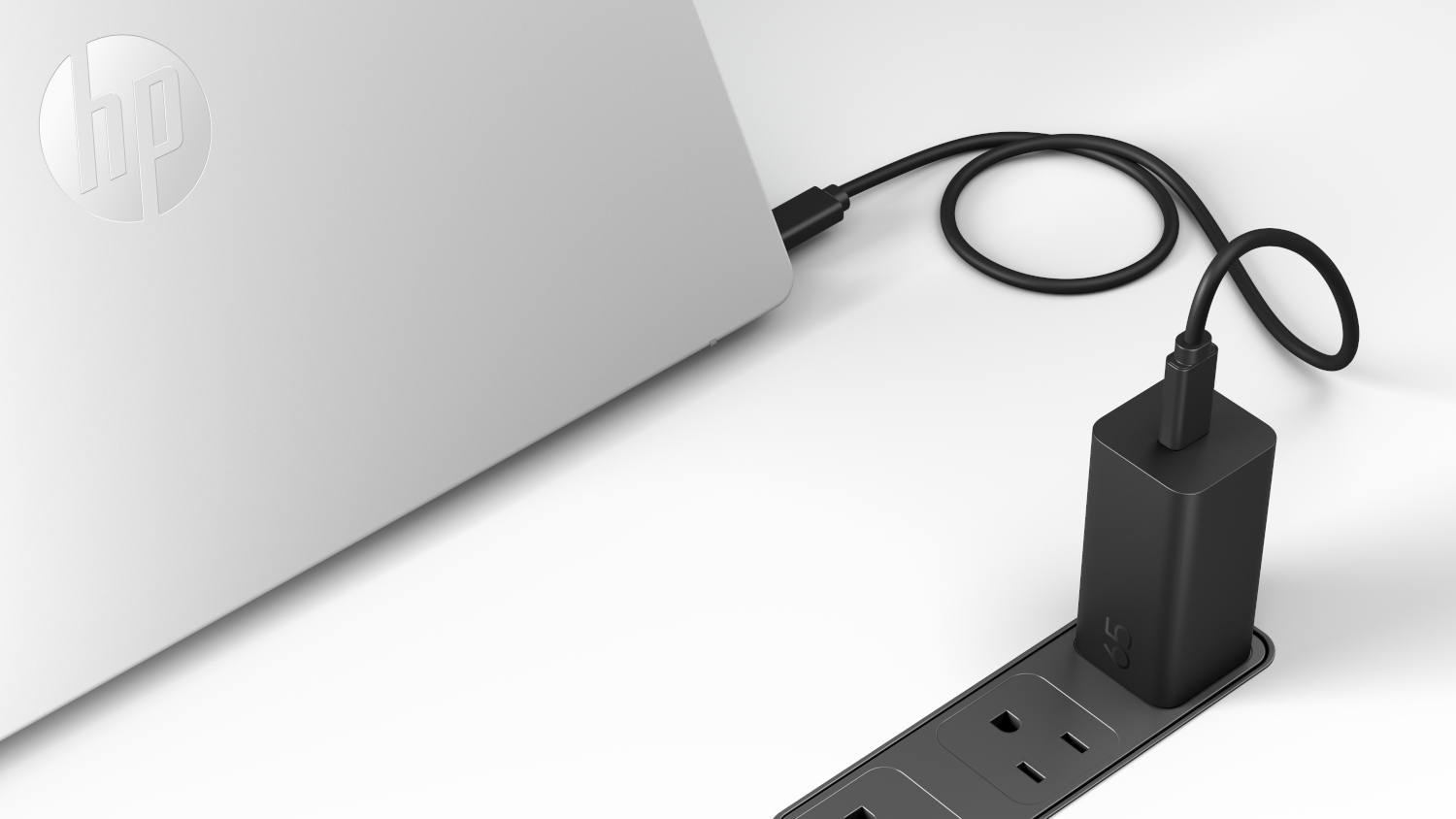 Een zwarte 65W lader is aangesloten op een stekkerdoos, laadt een laptop op.