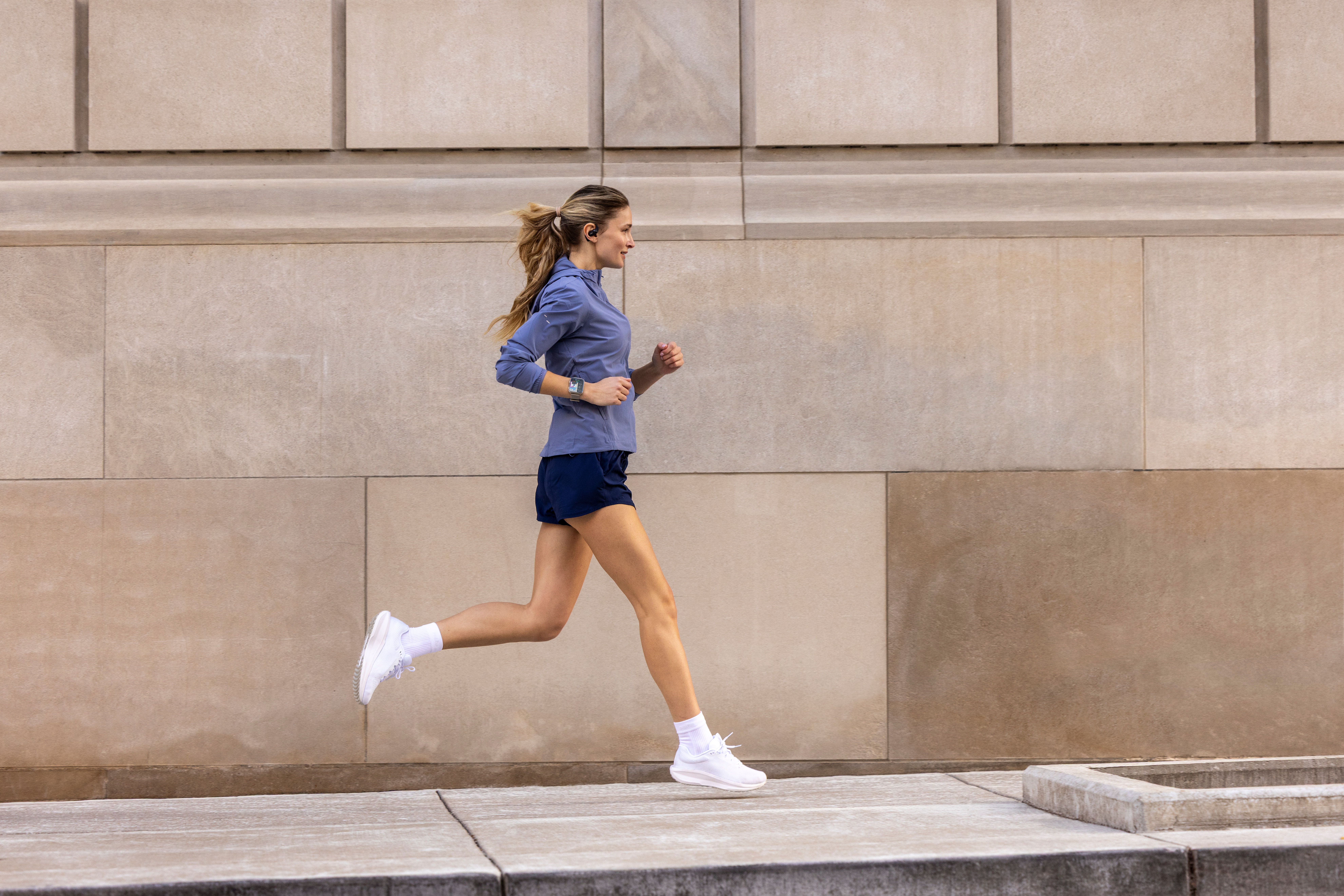 Eine Frau mit Pferdeschwanz läuft in blauer Sportkleidung auf einem Gehweg.