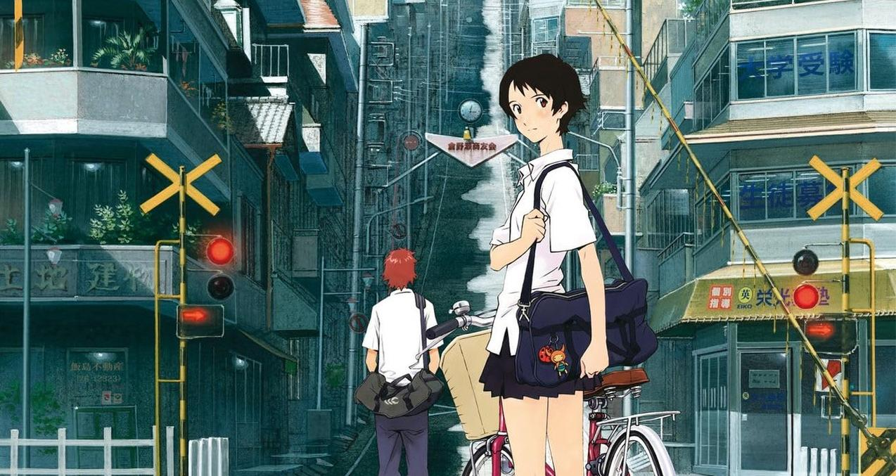Zwei Schüler stehen vor einer Eisenbahnkreuzung in einer Stadt. Ein Mädchen mit Fahrrad, ein Junge geht.