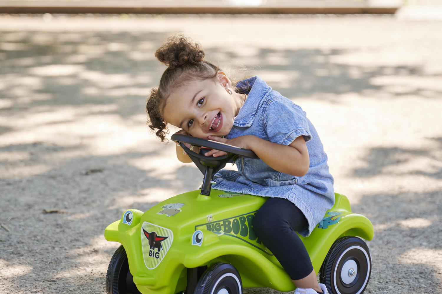 Ein kleines Mädchen mit zerzaustem Haar sitzt auf einem grünen Spielzeugauto.