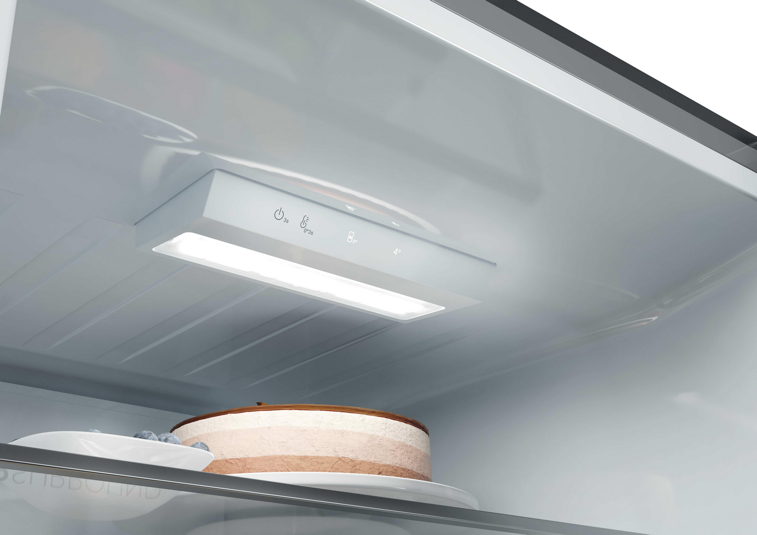 Un pastel en capas y arándanos dentro de un refrigerador con iluminación LED.