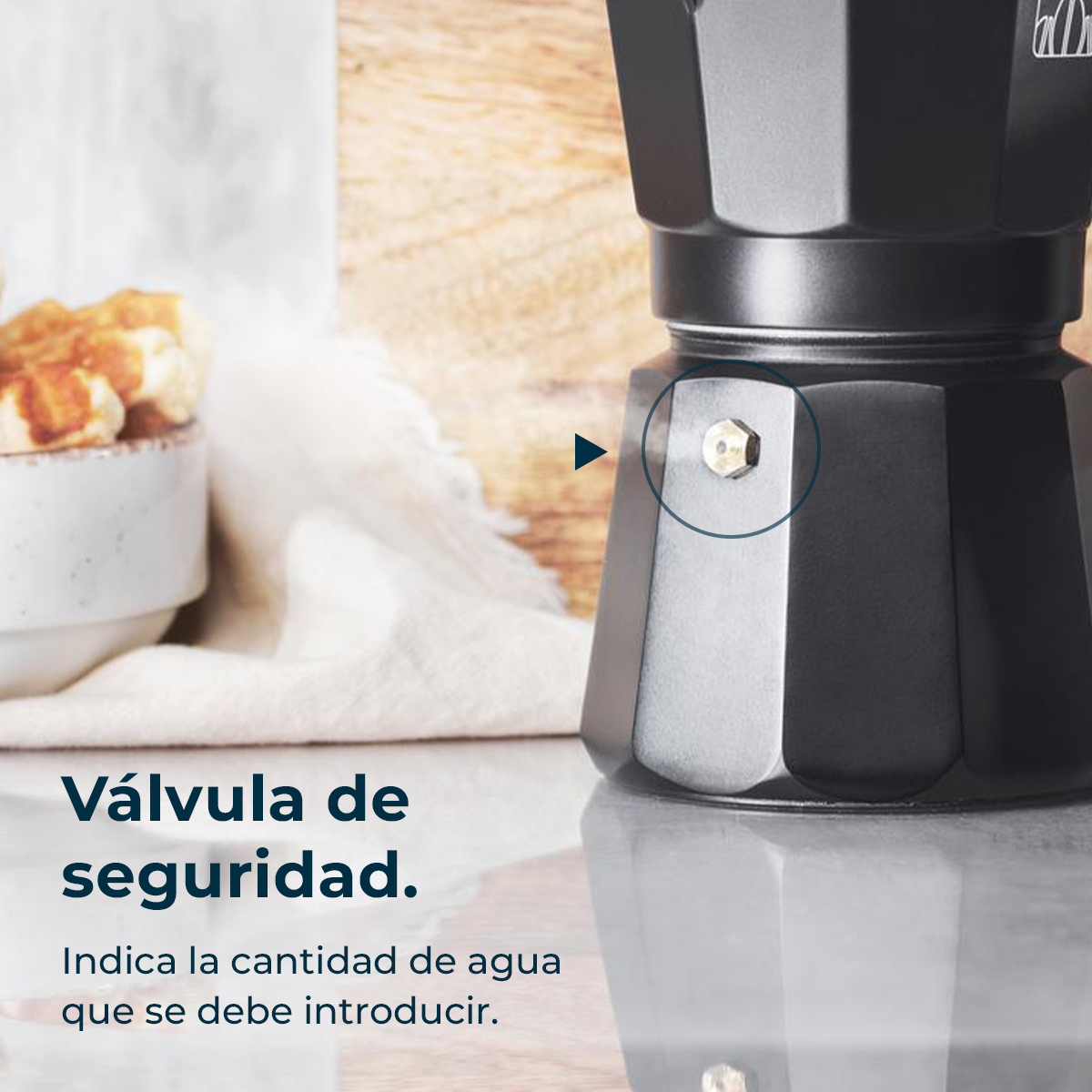 Una cafetera moka negra con válvula de seguridad. A la izquierda hay gofres.