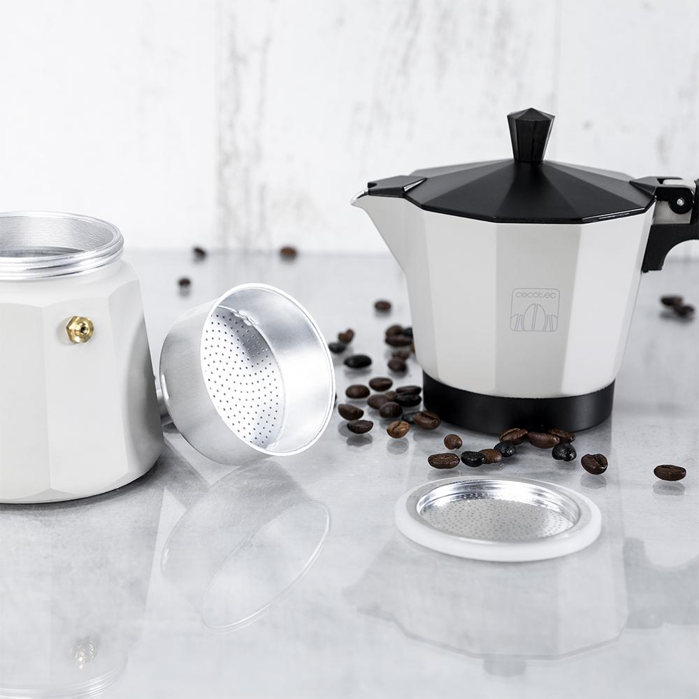 Una cafetera moka blanca con tapa negra y granos de café esparcidos.