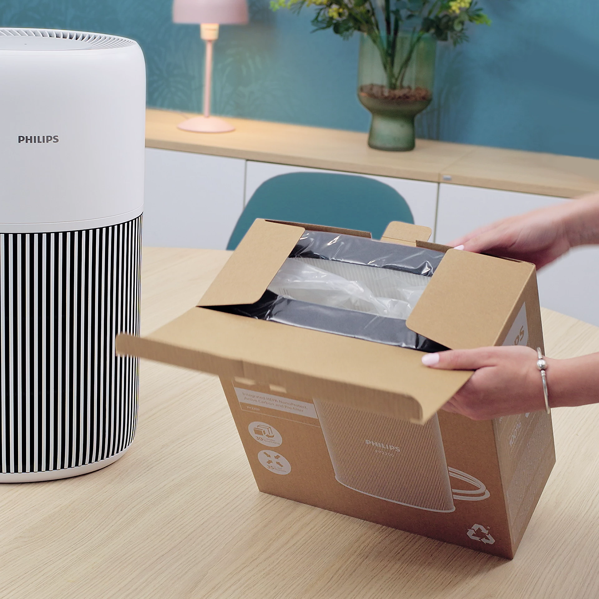 Egy személy egy Philips légtisztító dobozát nyitja ki a készülék mellett.