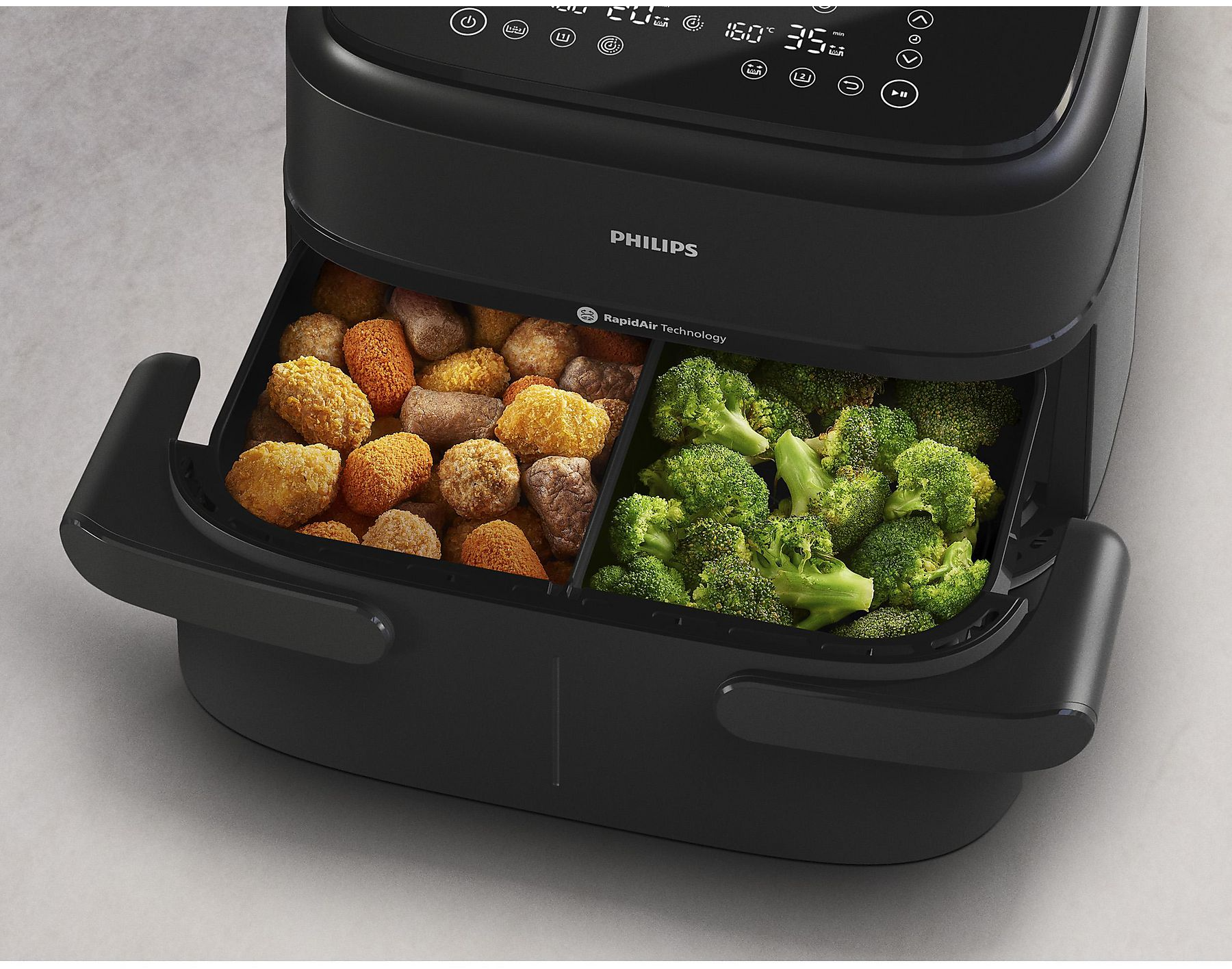 Egy fekete Philips légkeveréses fritőző két rekesszel, töltve nuggettel és brokkolival.