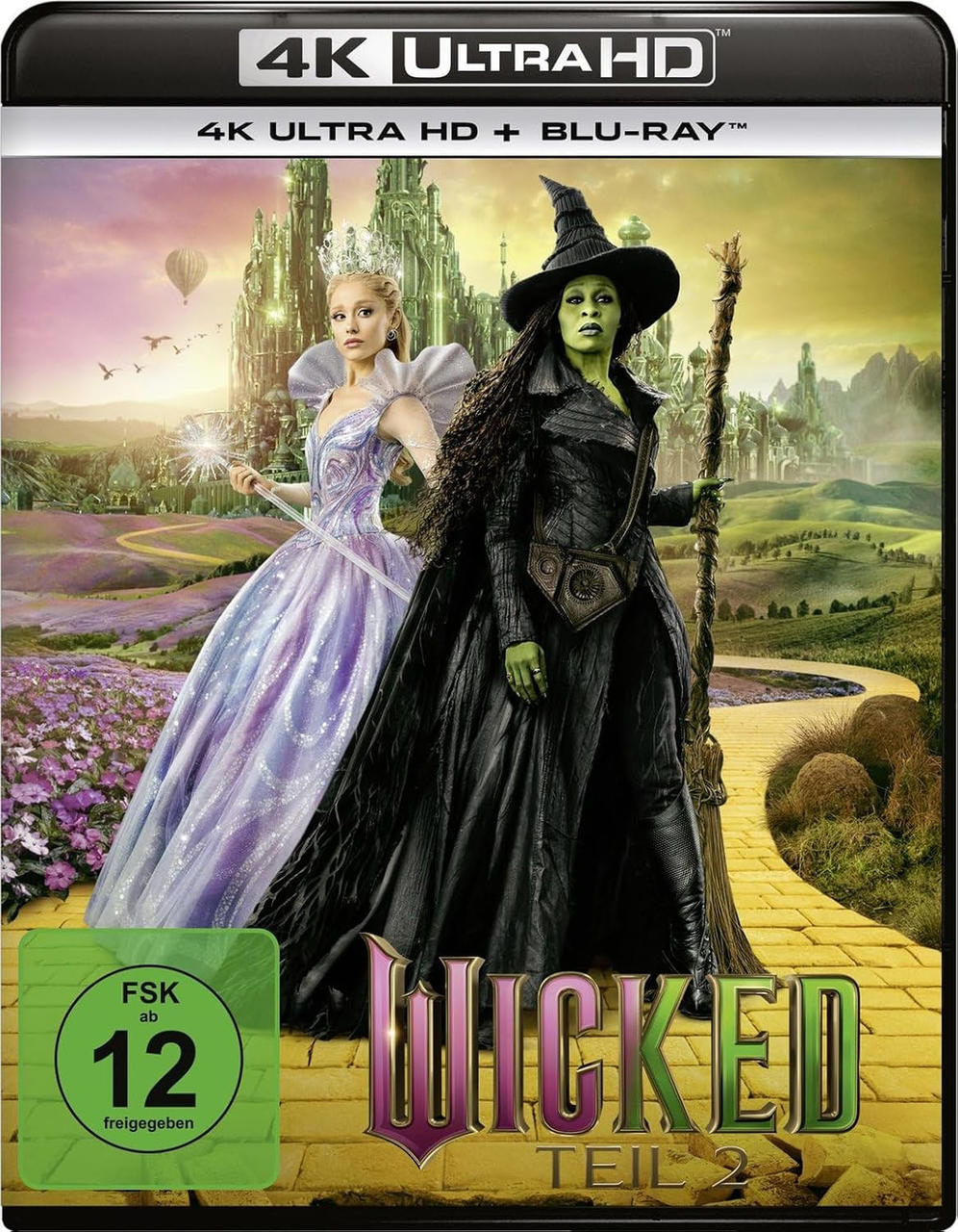 Zwei Hexen stehen vor einer smaragdgrünen Stadt. Eine trägt ein lila Kleid, die andere schwarz.