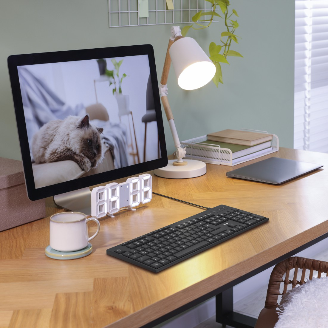 Schreibtisch mit Computer, Tastatur, Becher, Lampe und Katze auf dem Bildschirm.
