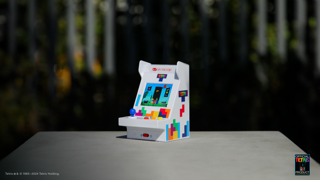 Mavi kumandalı beyaz Tetris mini atari oyunu gri yüzeyde duruyor.