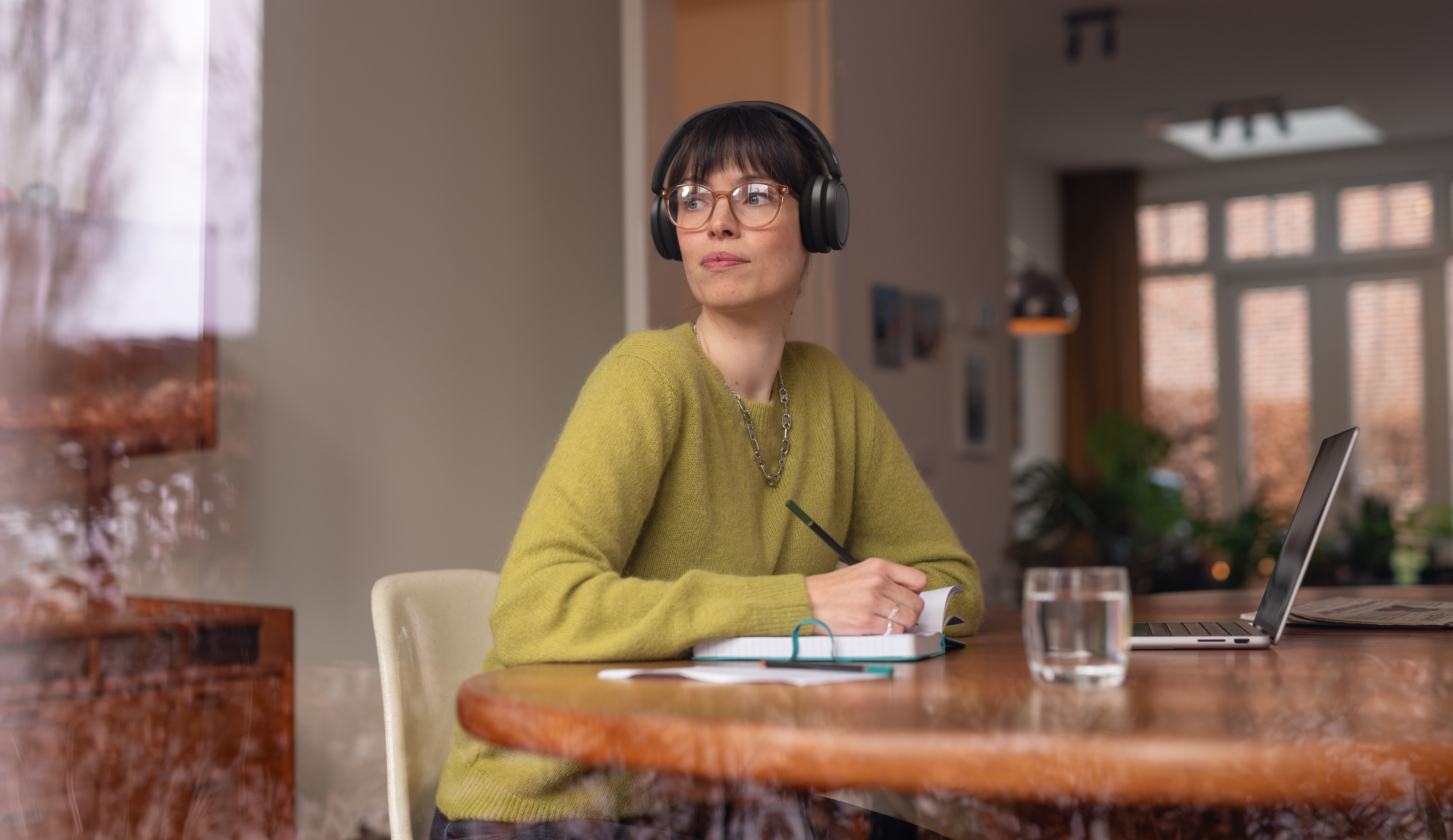 Eine Frau mit Kopfhörern schreibt in ein Notizbuch, während sie am Tisch sitzt.