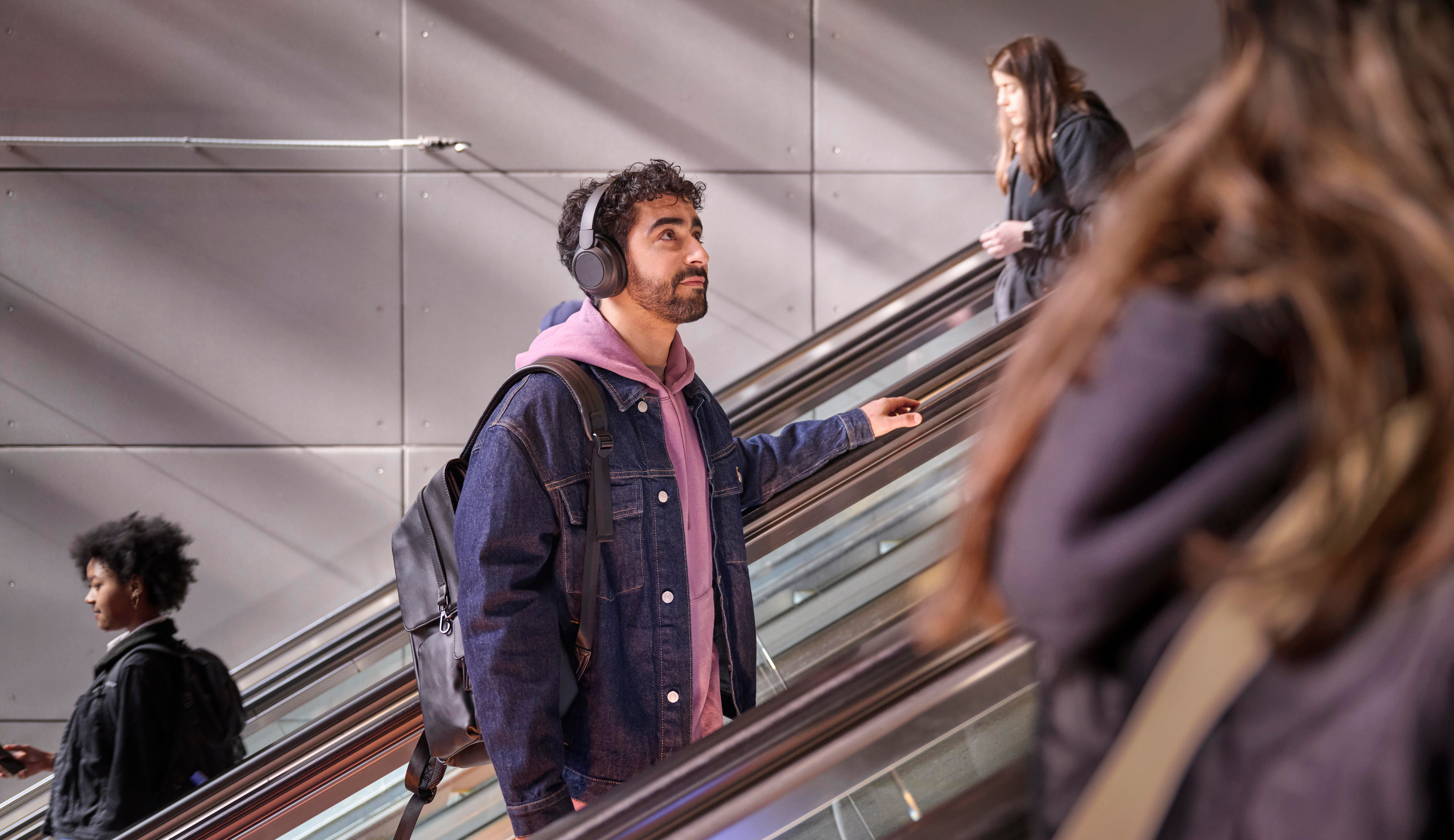 Mann mit Kopfhörern und Rucksack fährt Rolltreppe hoch.