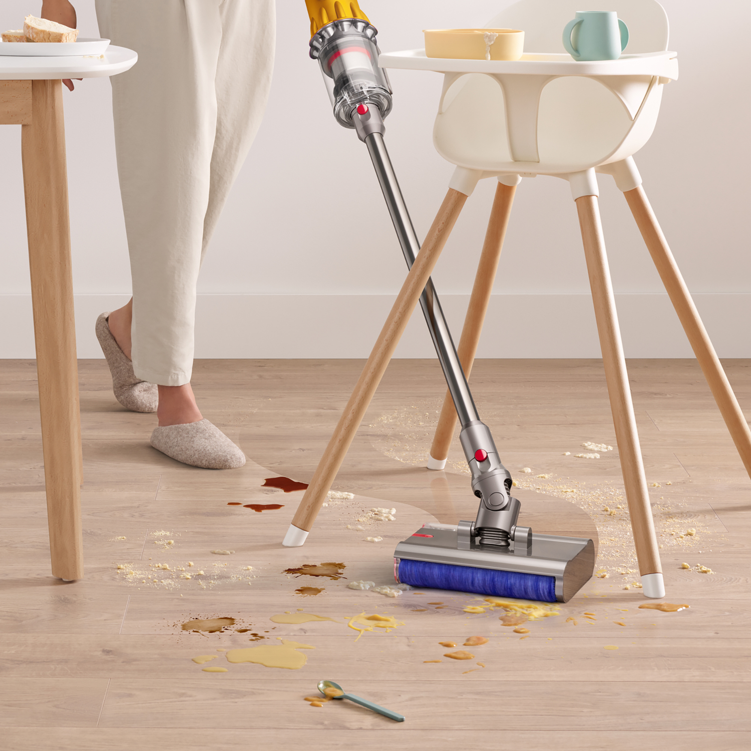 A vacuum cleaner cleans spills and crumbs on a wooden floor next to a high chair.