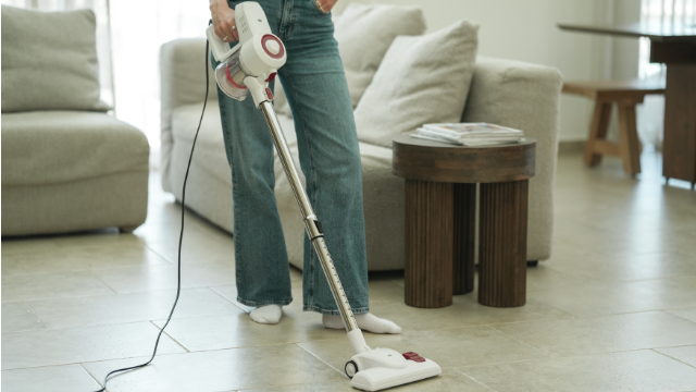 Une personne en jean passe l'aspirateur sur un sol carrelé avec un aspirateur blanc.