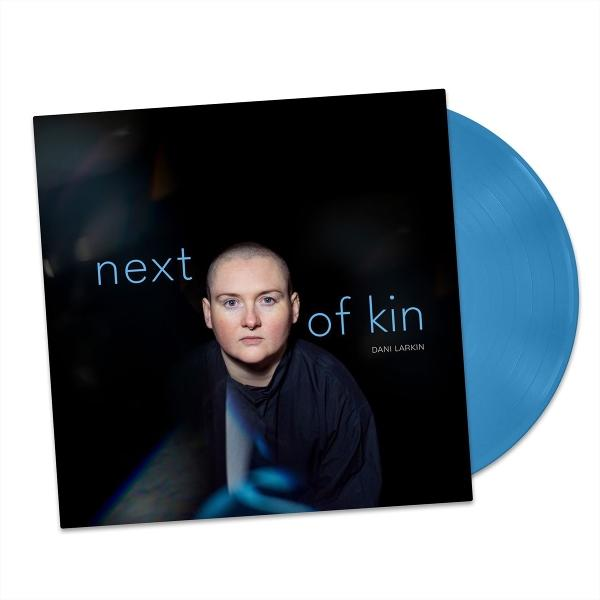 Ein blaues Vinyl-Albumcover mit einem Porträt einer Person mit kurzgeschorenen Haaren. Text: 'next of kin'.
