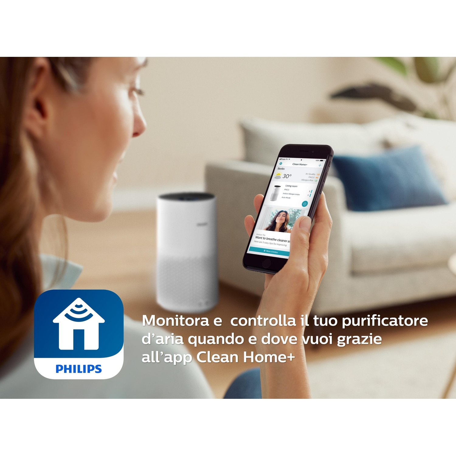 Una donna tiene uno smartphone con l'app Clean Home+. Un purificatore d'aria è nelle vicinanze.